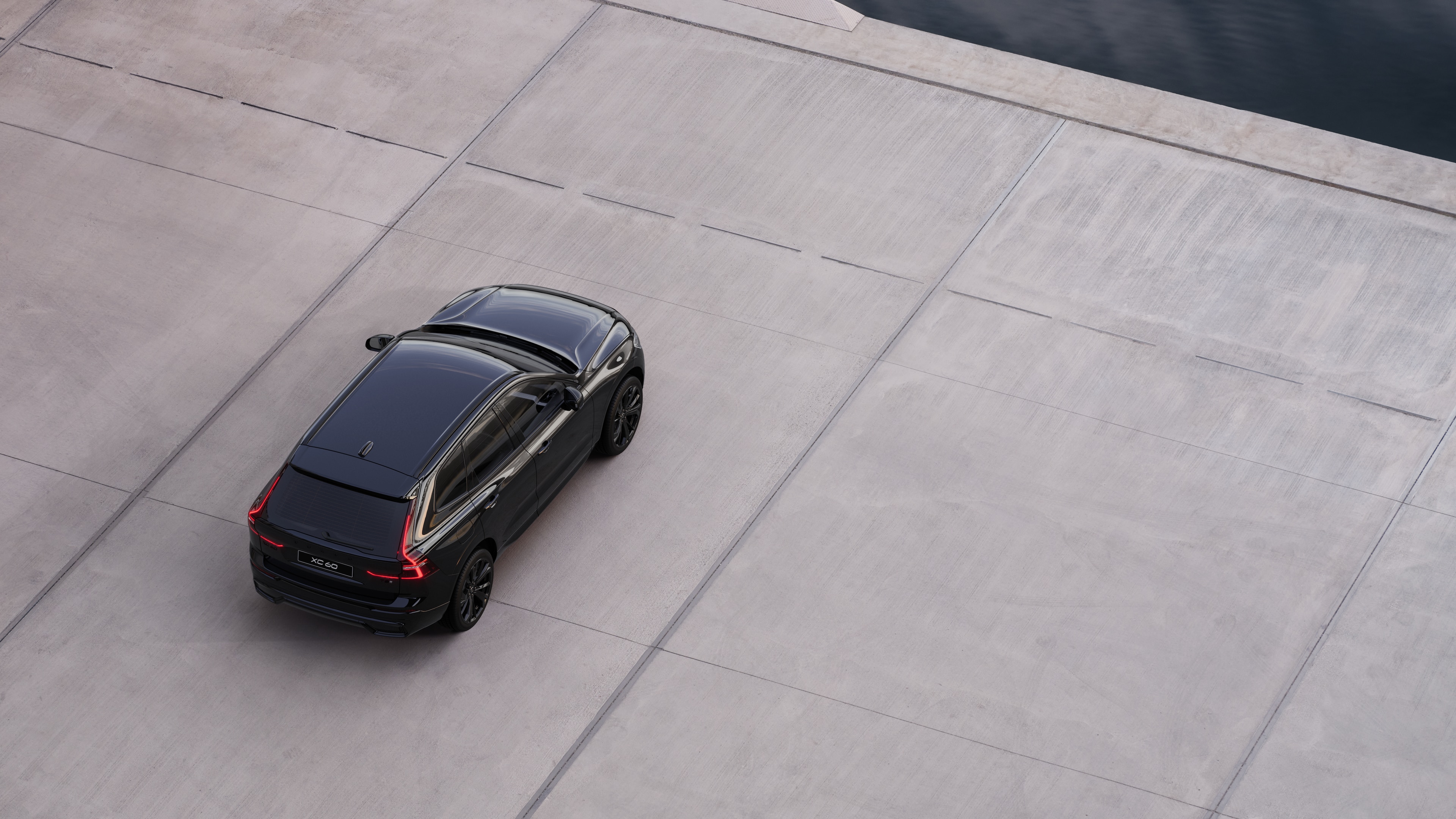 Volvo-auto takaa pysäköitynä hiljaiselle kadulle veden äärelle, taustalla päällystetty kävelytie ja vesi.