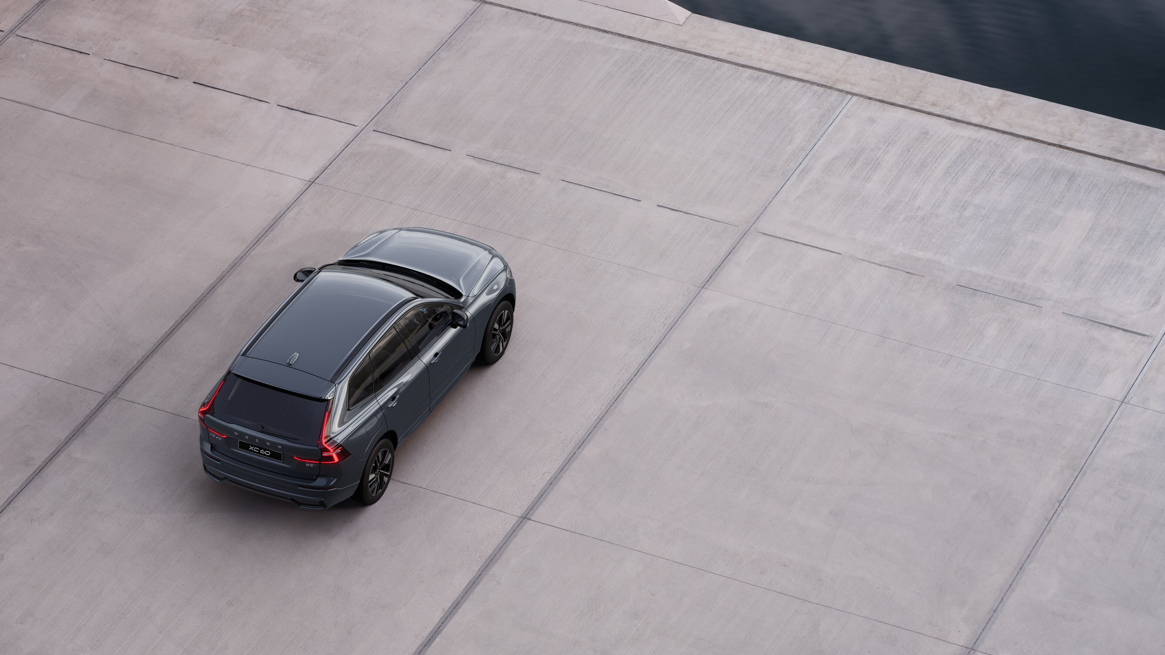 Volvo car rear view parked on quiet street beside water, with a paved walkway and water as the background.