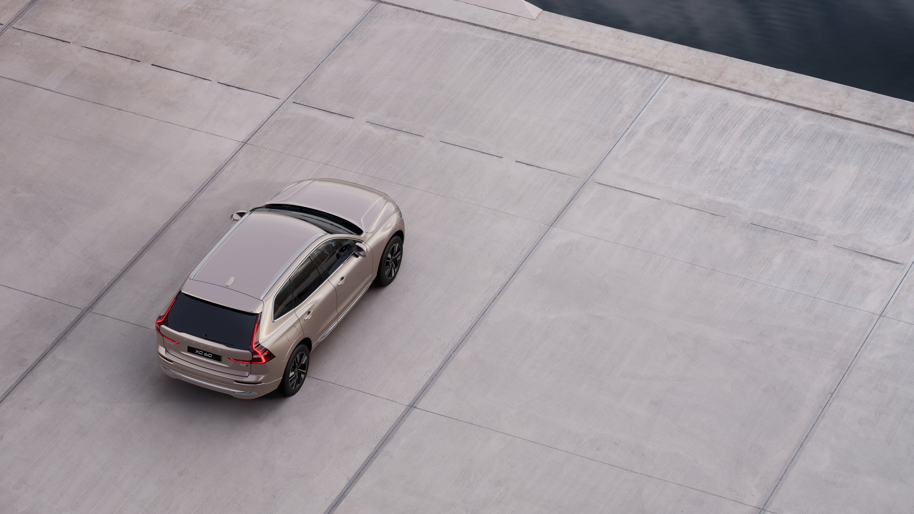 Volvo car rear view parked on quiet street beside water, with a paved walkway and water as the background.