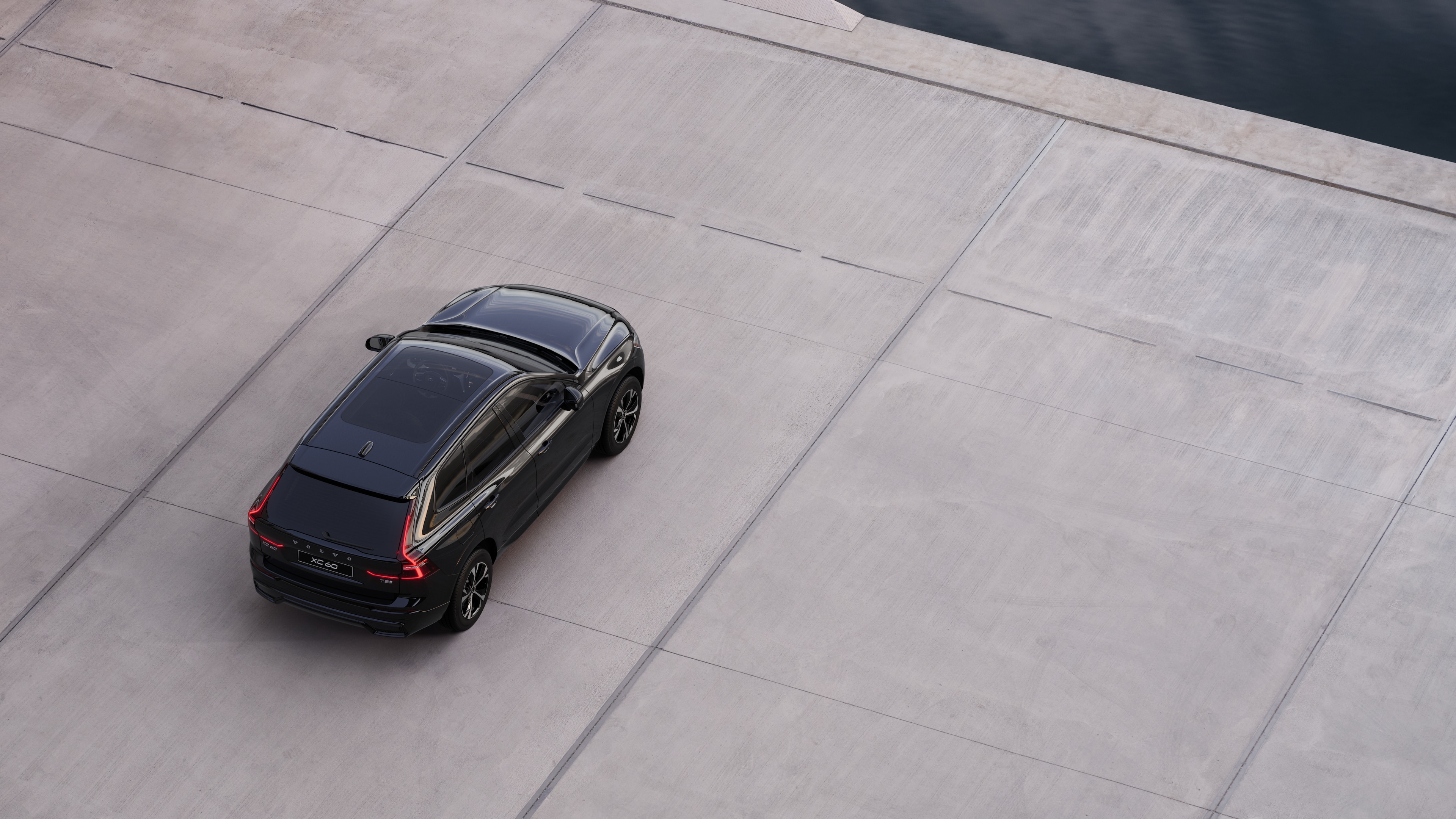 Volvo car rear view parked on quiet street beside water, with a paved walkway and water as the background.