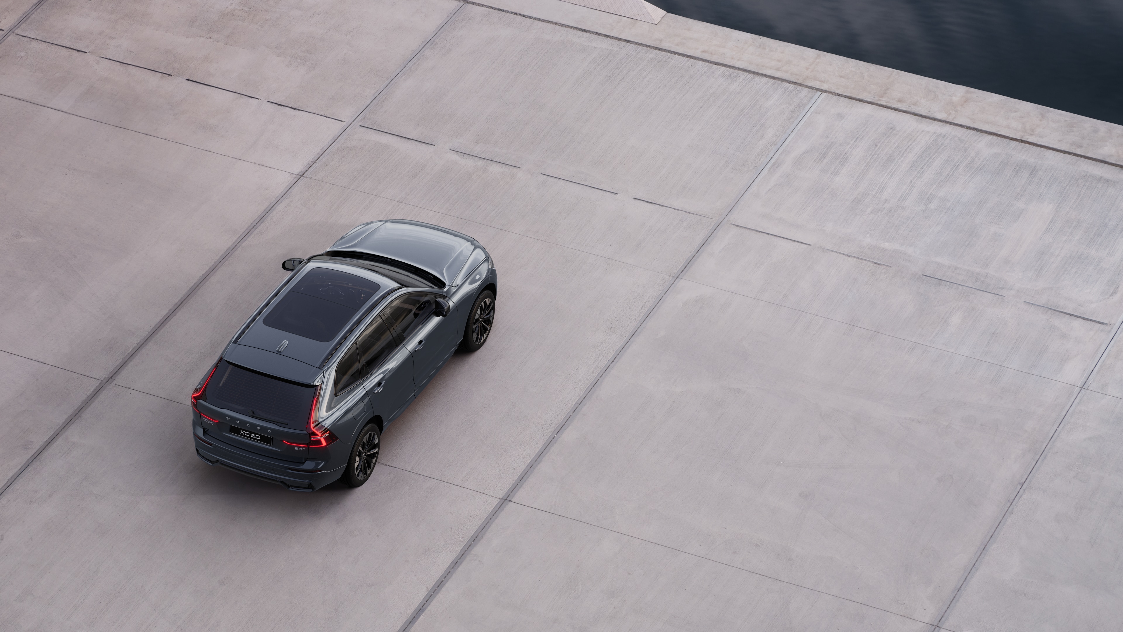 Автомобиль Volvo, вид сзади, припаркованный на тихой улице рядом с водой, на фоне мощеной дорожки и воды.