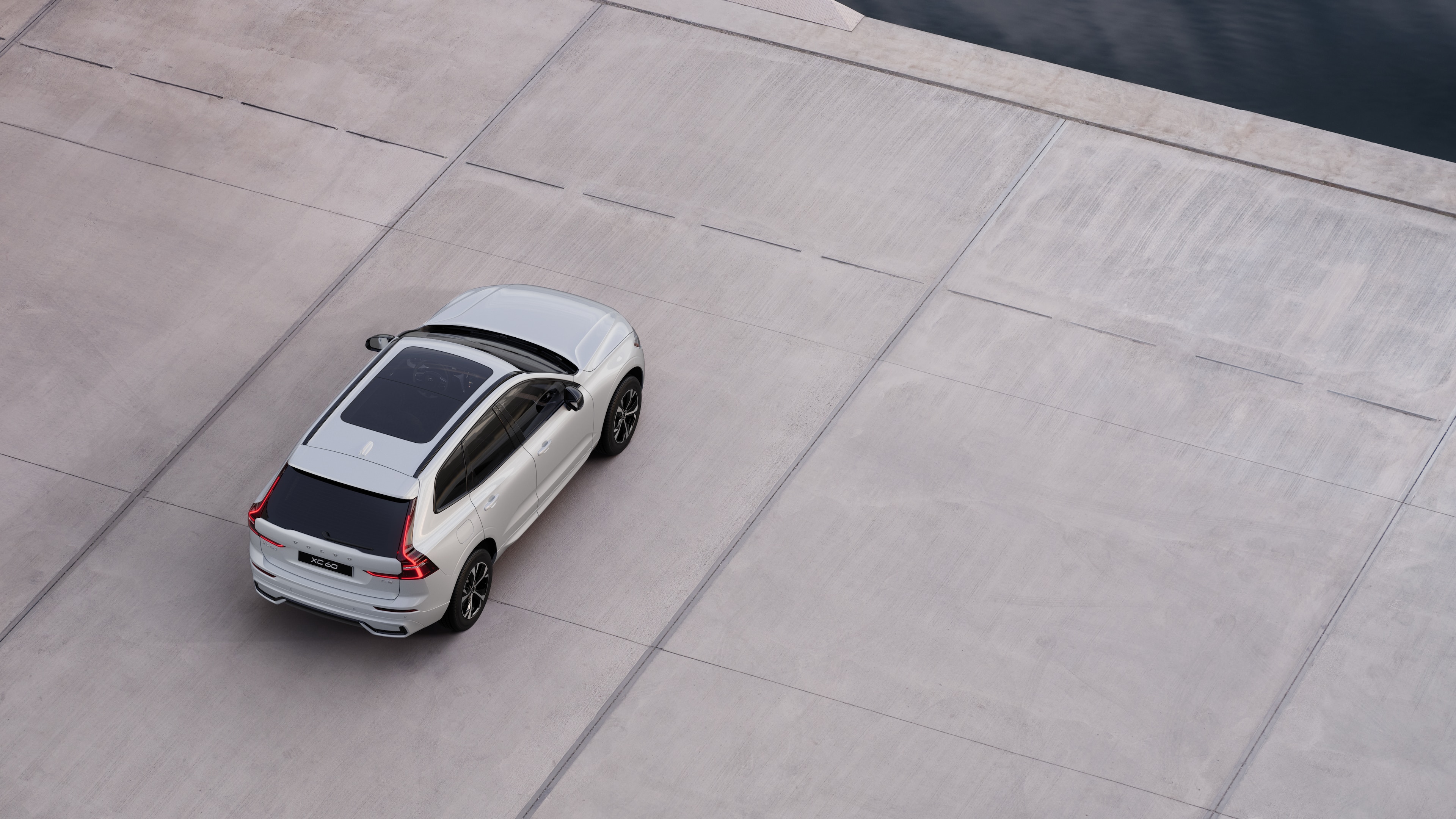 Volvo car rear view parked on quiet street beside water, with a paved walkway and water as the background.