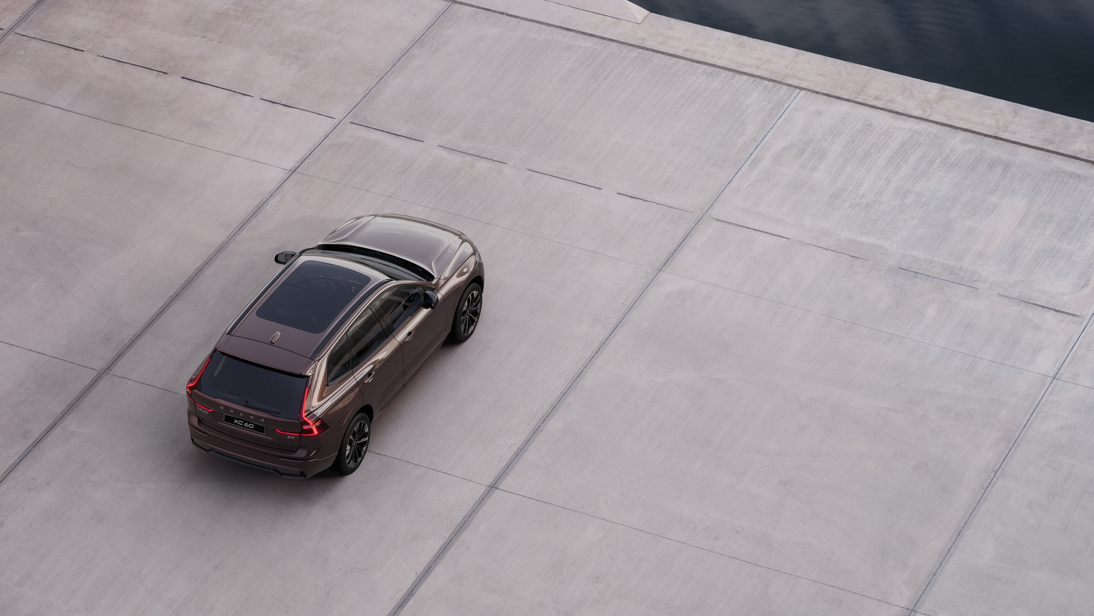 Автомобиль Volvo, вид сзади, припаркованный на тихой улице рядом с водой, на фоне мощеной дорожки и воды.