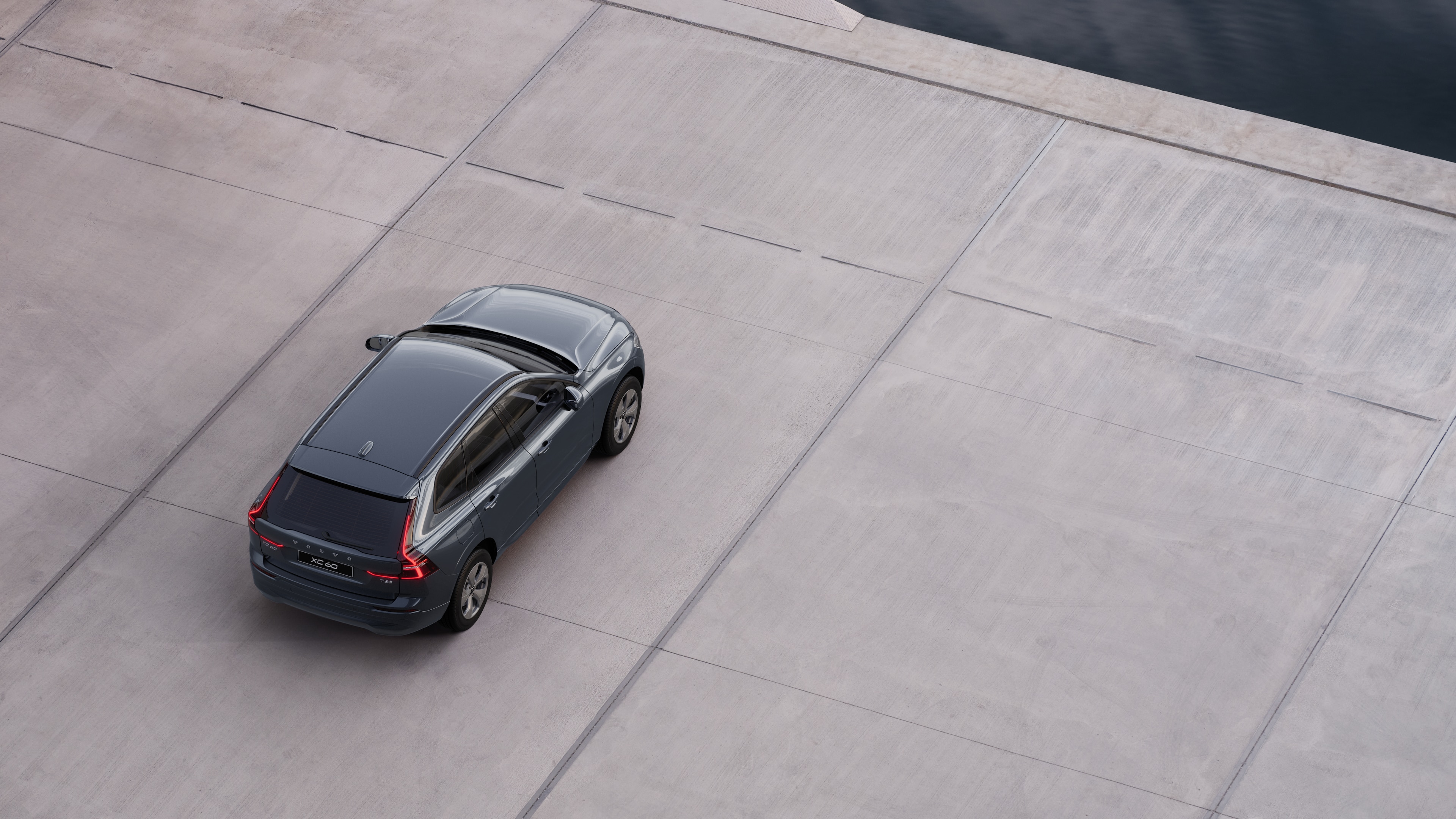 Vista posteriore di un'auto Volvo parcheggiata in una strada tranquilla accanto all'acqua, con un passaggio pedonale lastricato e l'acqua sullo sfondo.