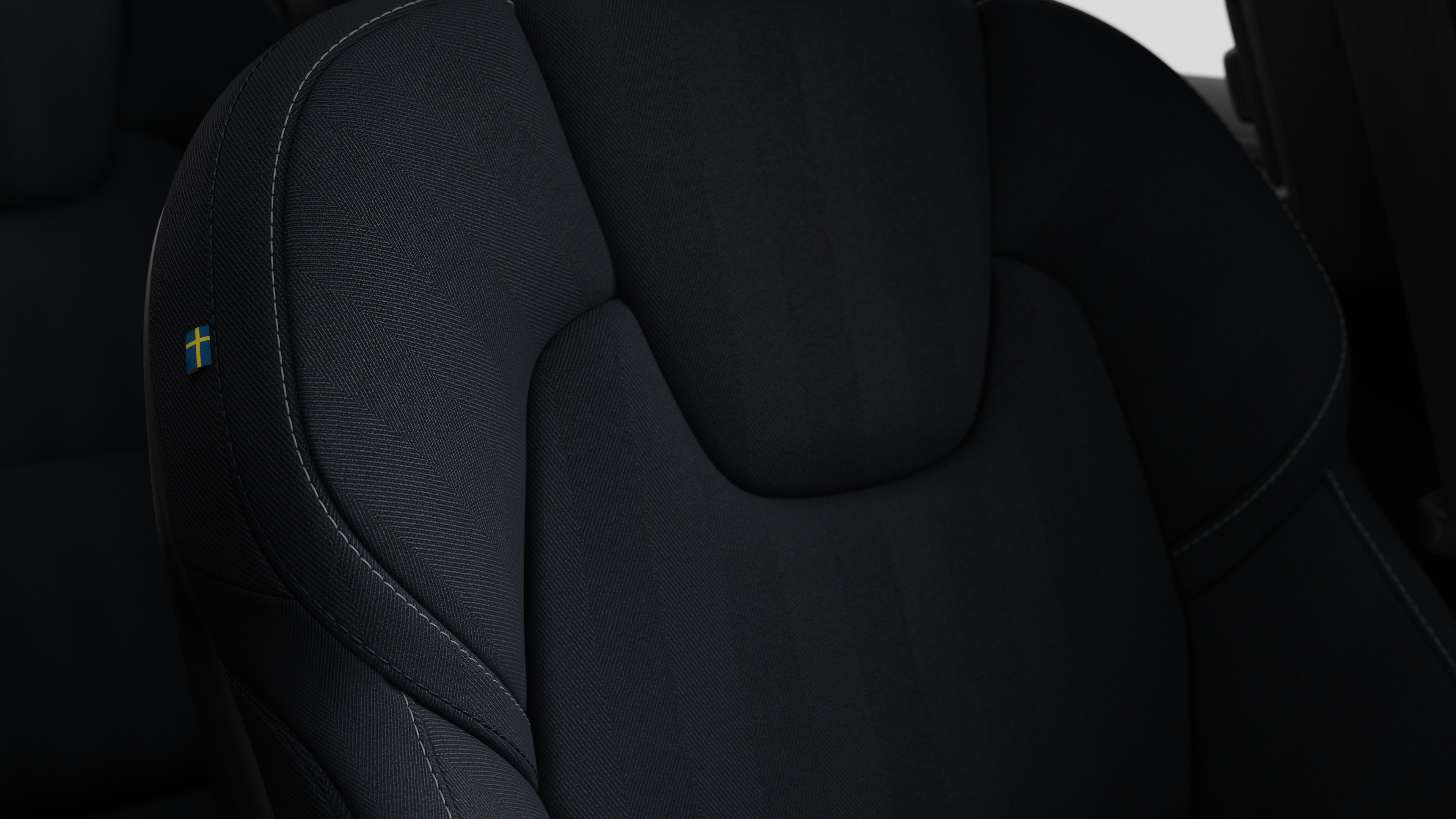 Close-up of Volvo car interior seat detail showing stitching and a small Swedish flag tag.