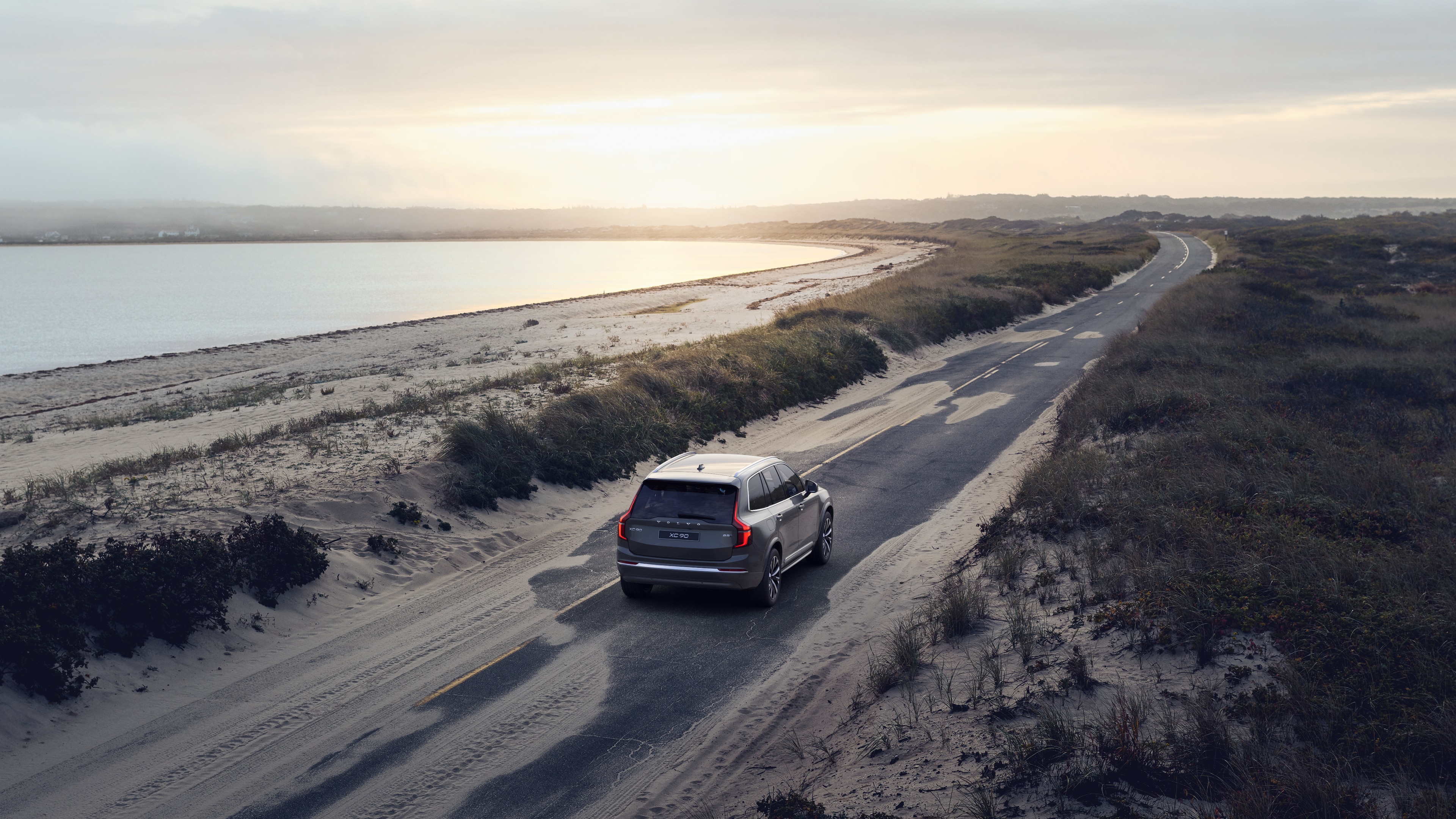 Volvo car rear view on a winding coastal road with a beachside background.