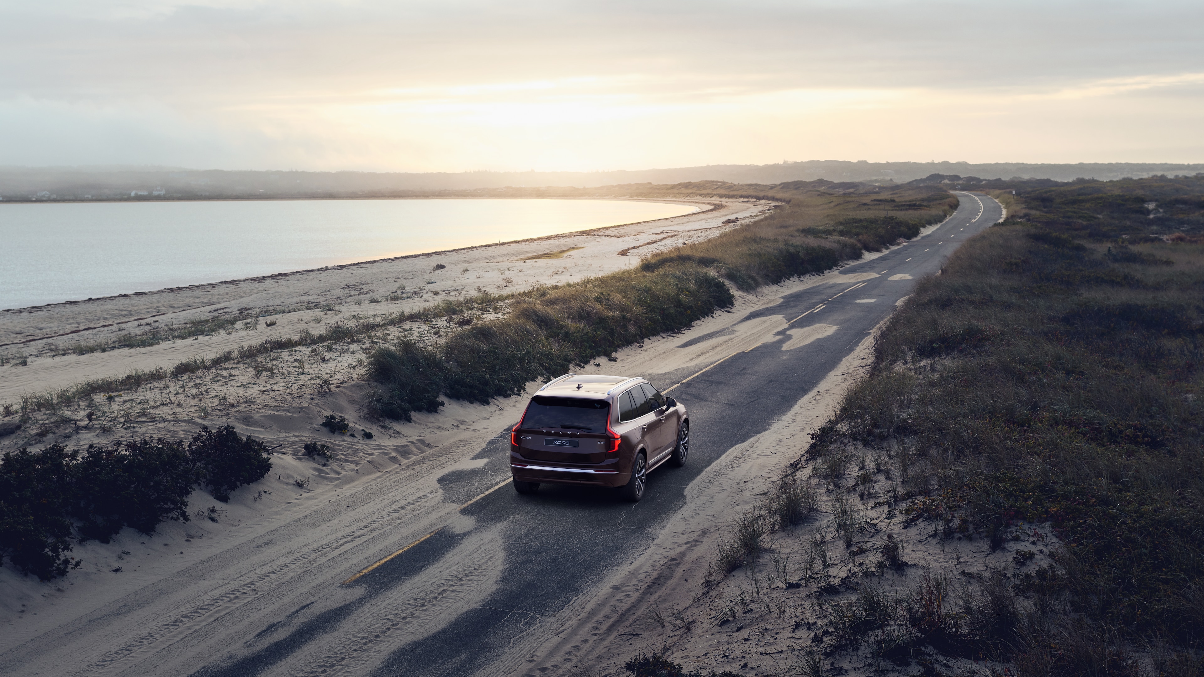 Volvo car rear view on a winding coastal road with a beachside background.