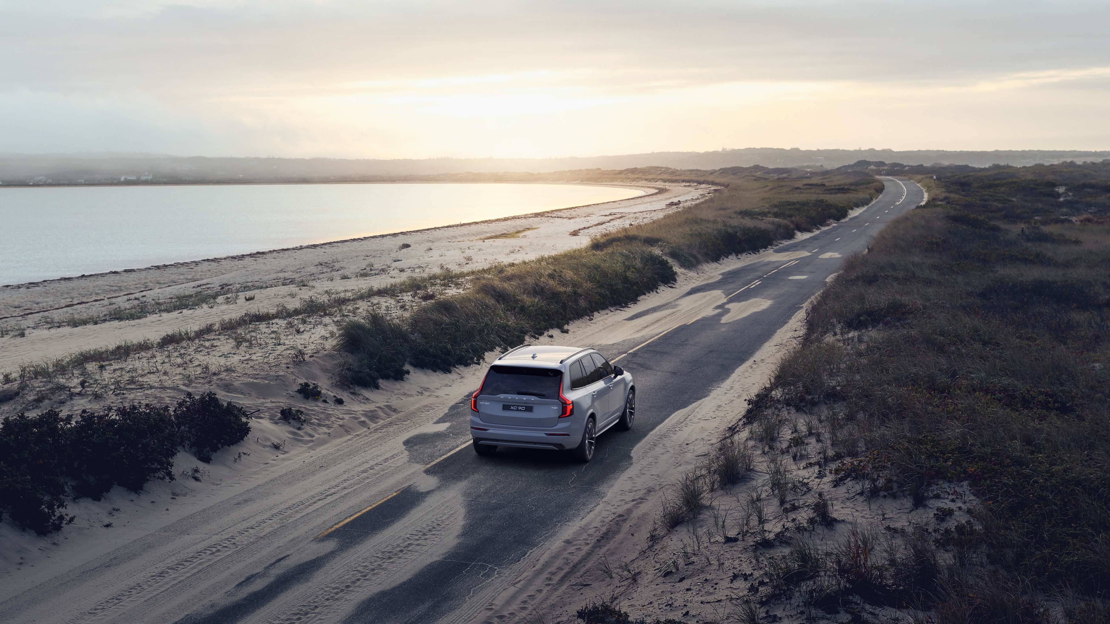 Vue arrière d’une Volvo sur une route côtière sinueuse avec un arrière-plan en bord de mer.