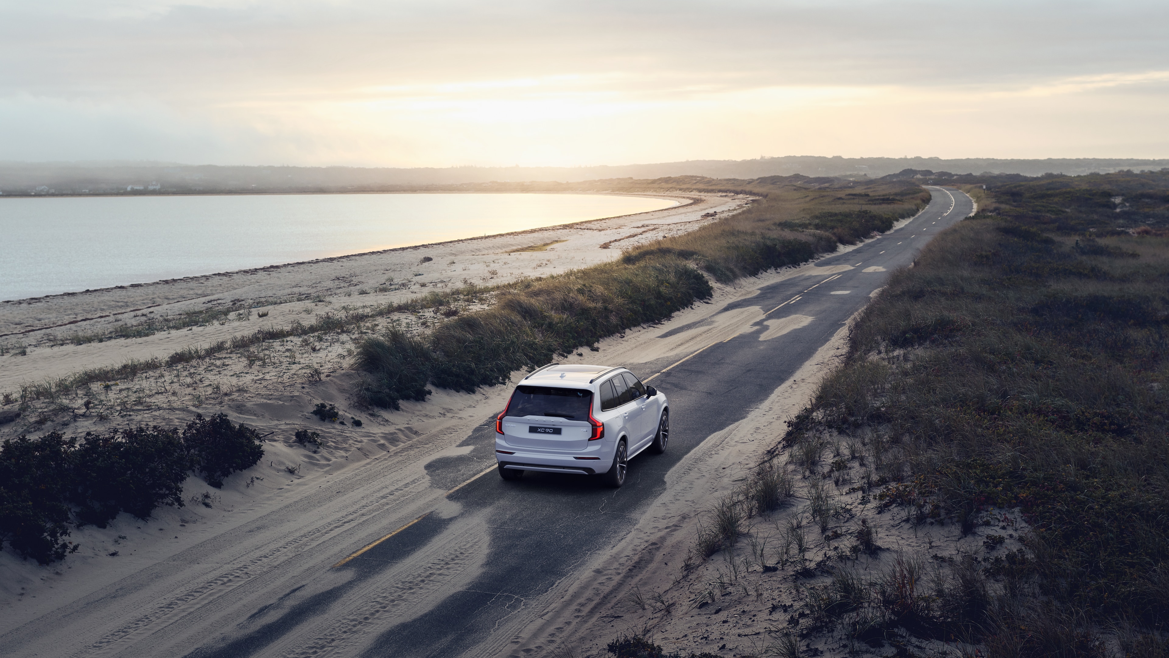 Stražnji pogled automobila Volvo na zavojitu obalnu cestu s pozadinom uz plažu.