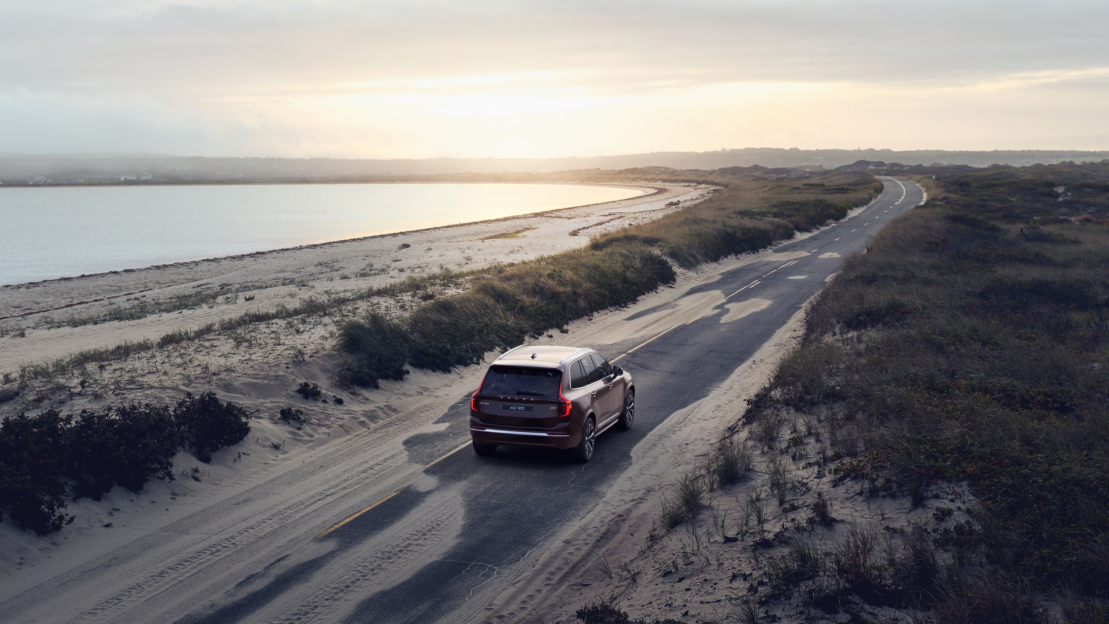 Stražnji pogled automobila Volvo na zavojitu obalnu cestu s pozadinom uz plažu.