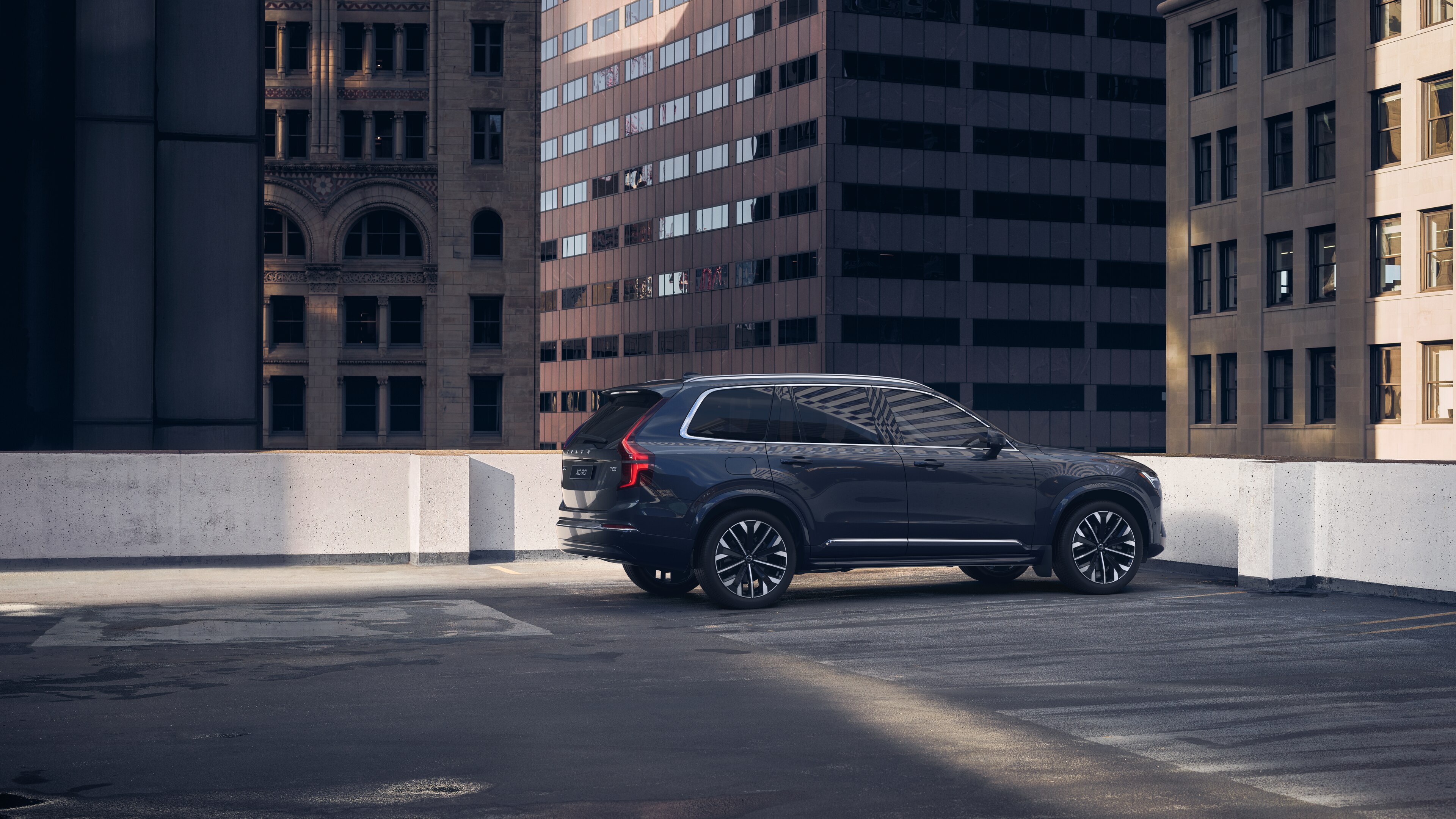Volvo car in rear three-quarter view on an urban rooftop parking lot with surrounding tall buildings.