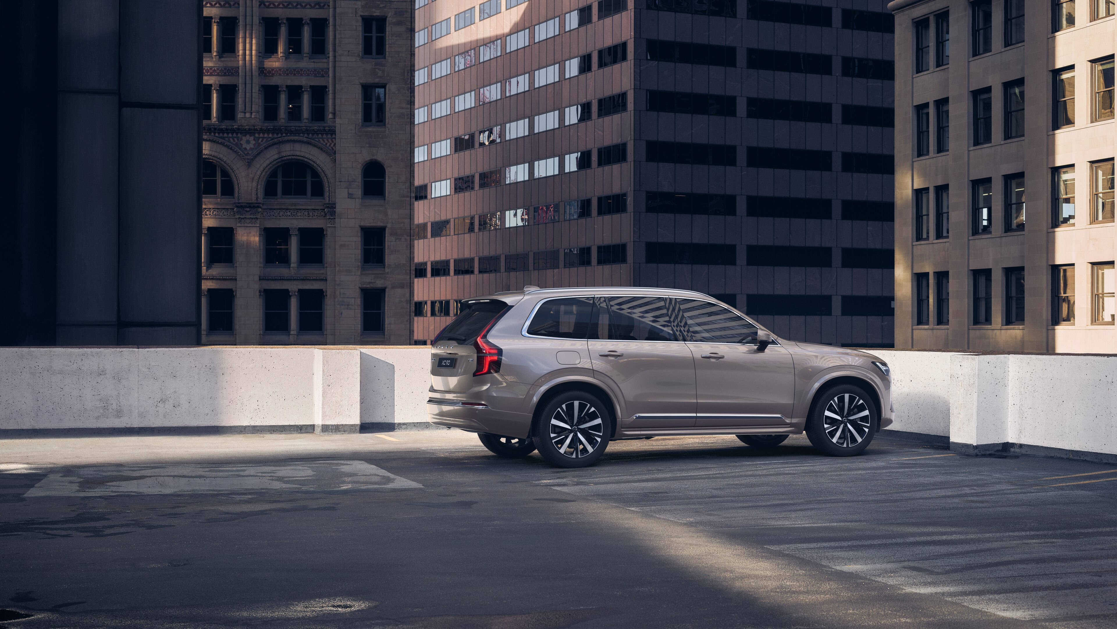 Una Volvo con vista posteriore di tre quarti su un parcheggio panoramico urbano con alti edifici circostanti.