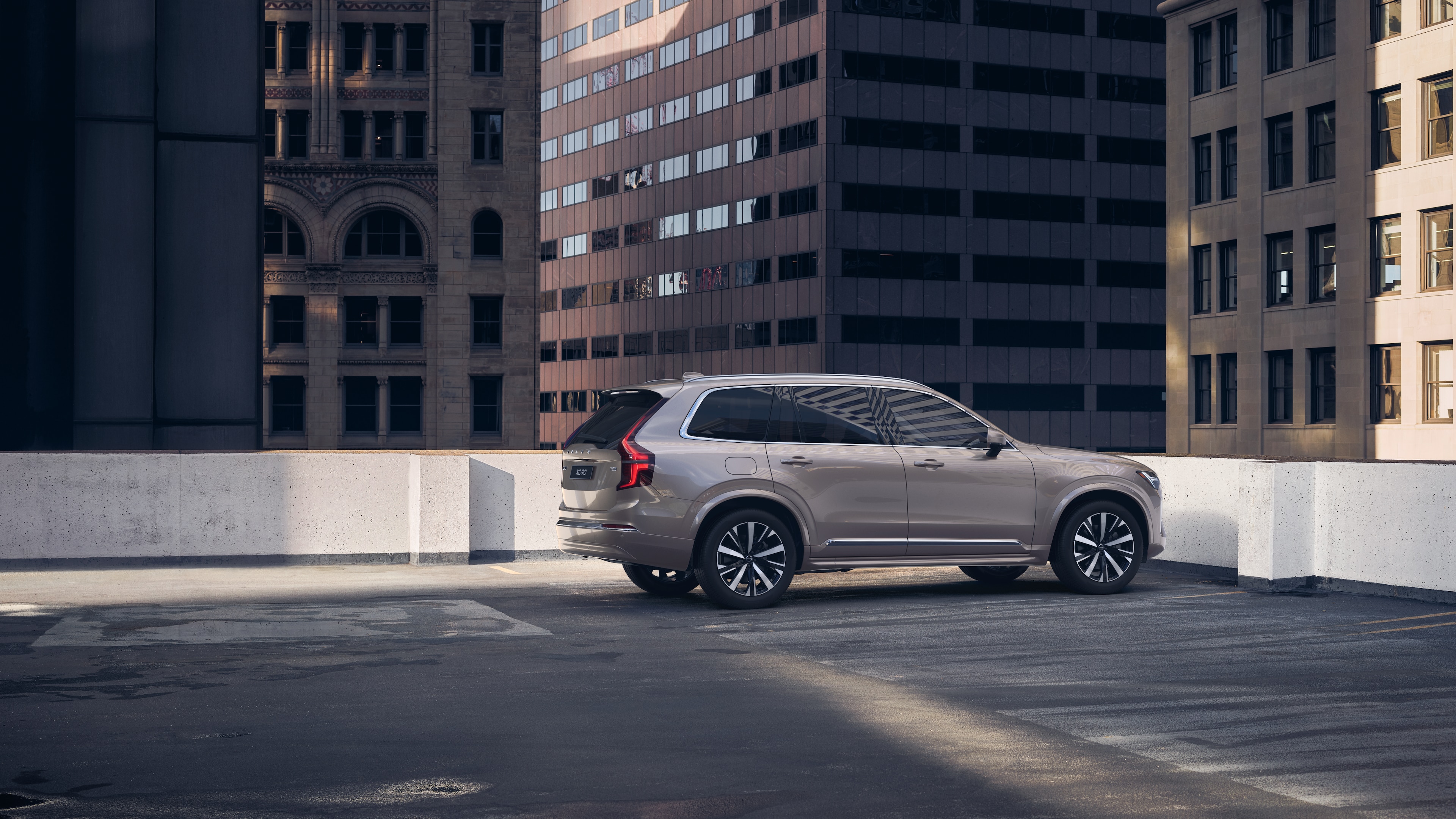 Volvo car in rear three-quarter view on an urban rooftop parking lot with surrounding tall buildings.