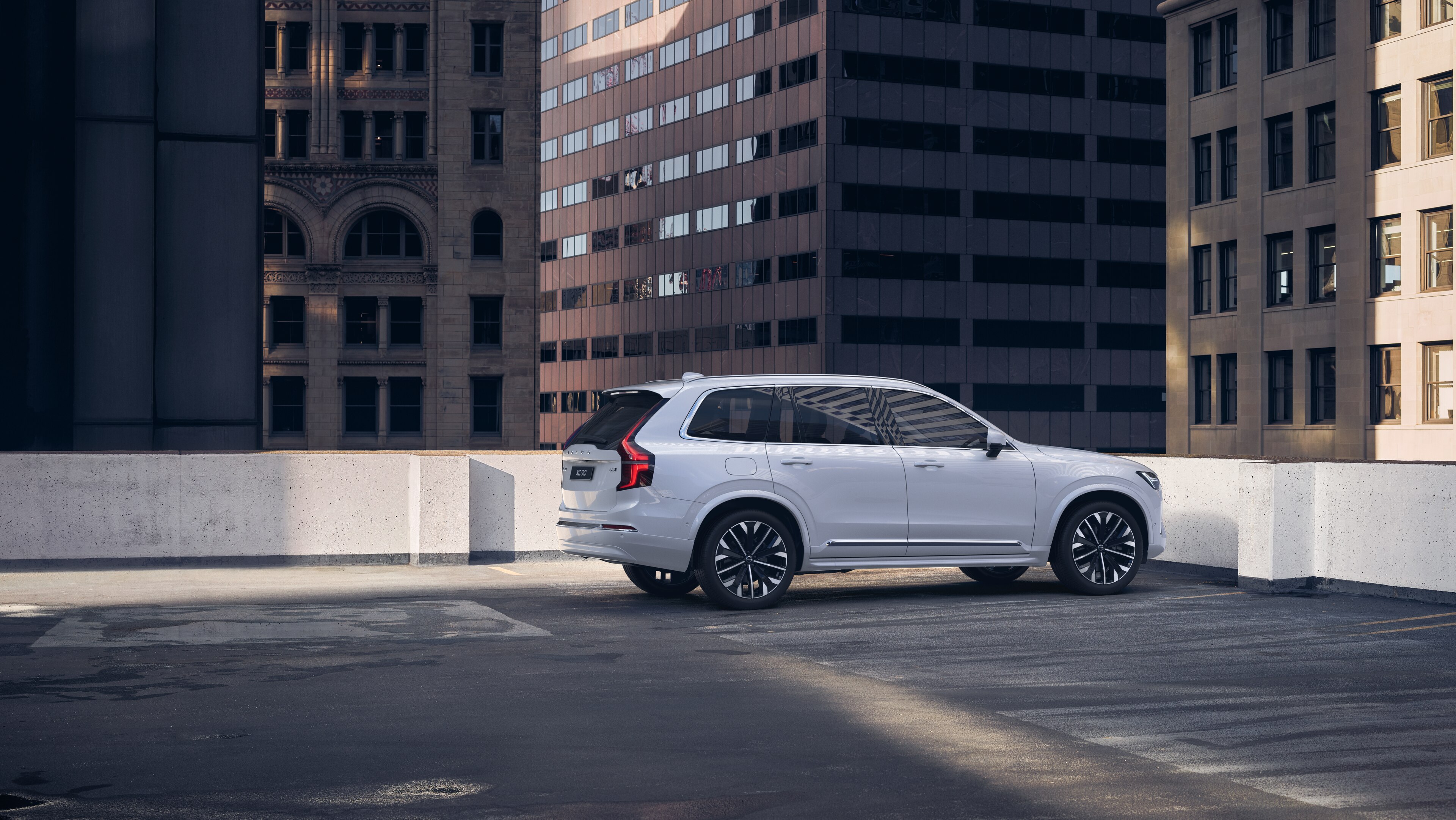 Una Volvo con vista posteriore di tre quarti su un parcheggio panoramico urbano con alti edifici circostanti.