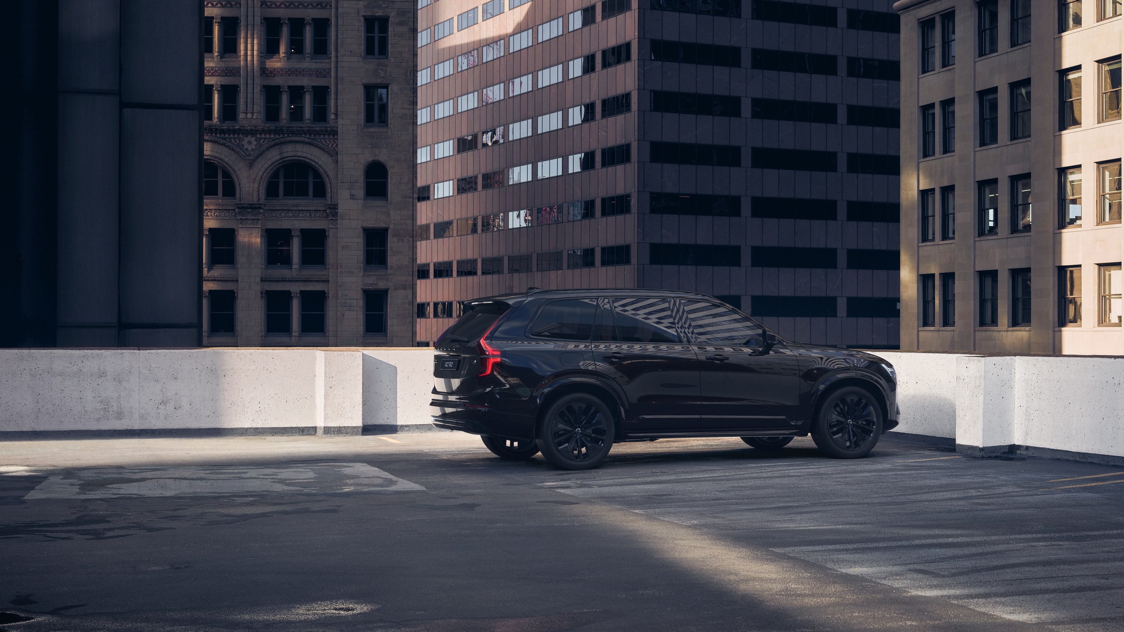 Volvo car in rear three-quarter view on an urban rooftop parking lot with surrounding tall buildings.