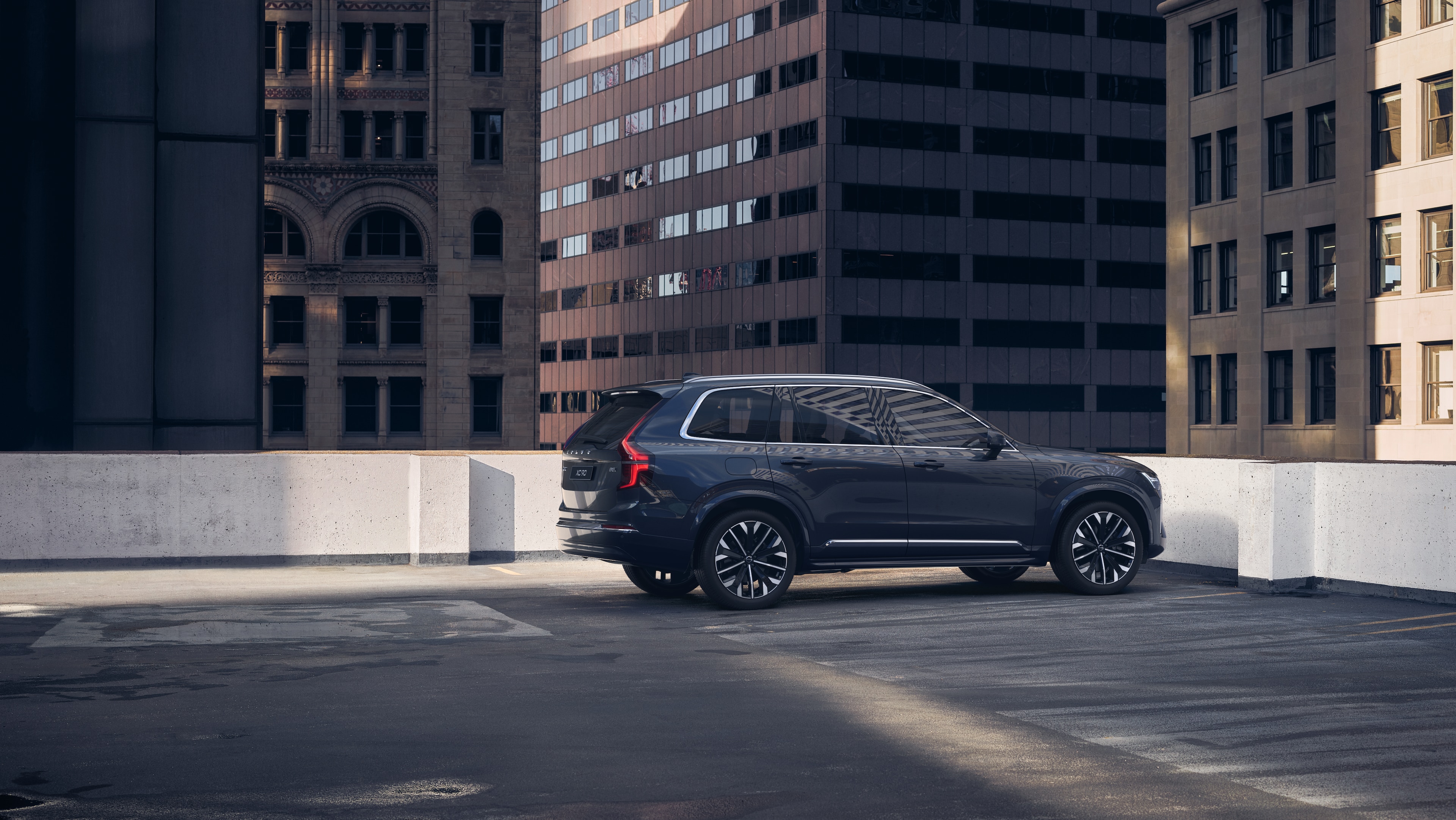 Una Volvo con vista posteriore di tre quarti su un parcheggio panoramico urbano con alti edifici circostanti.