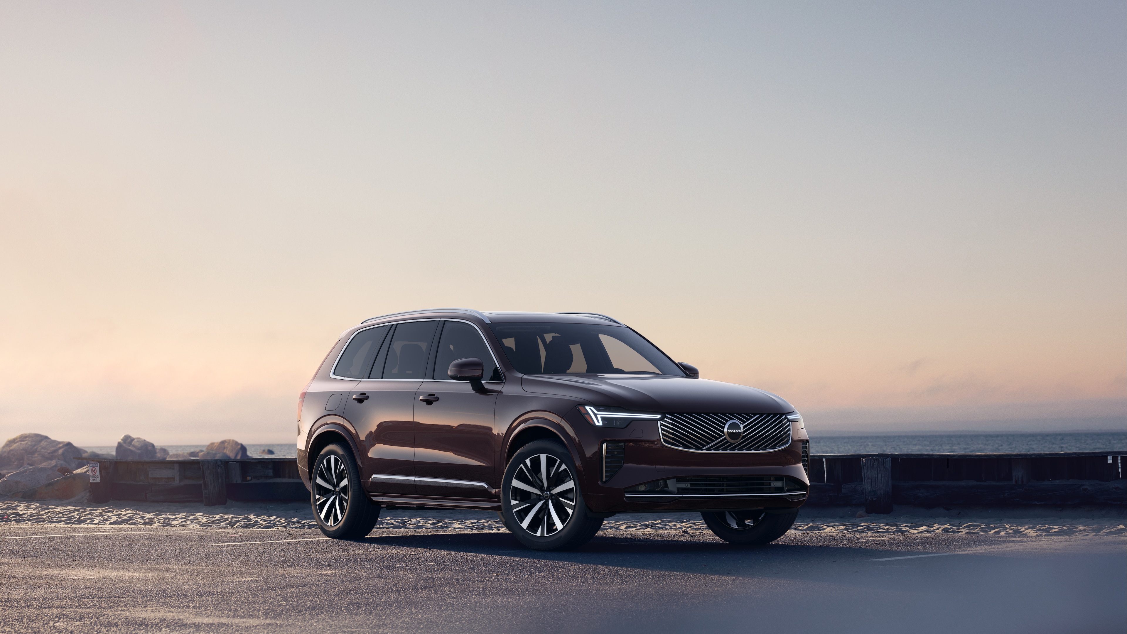 Volvo car in three-quarter view on coastal road, showing the front and side against a serene ocean background.