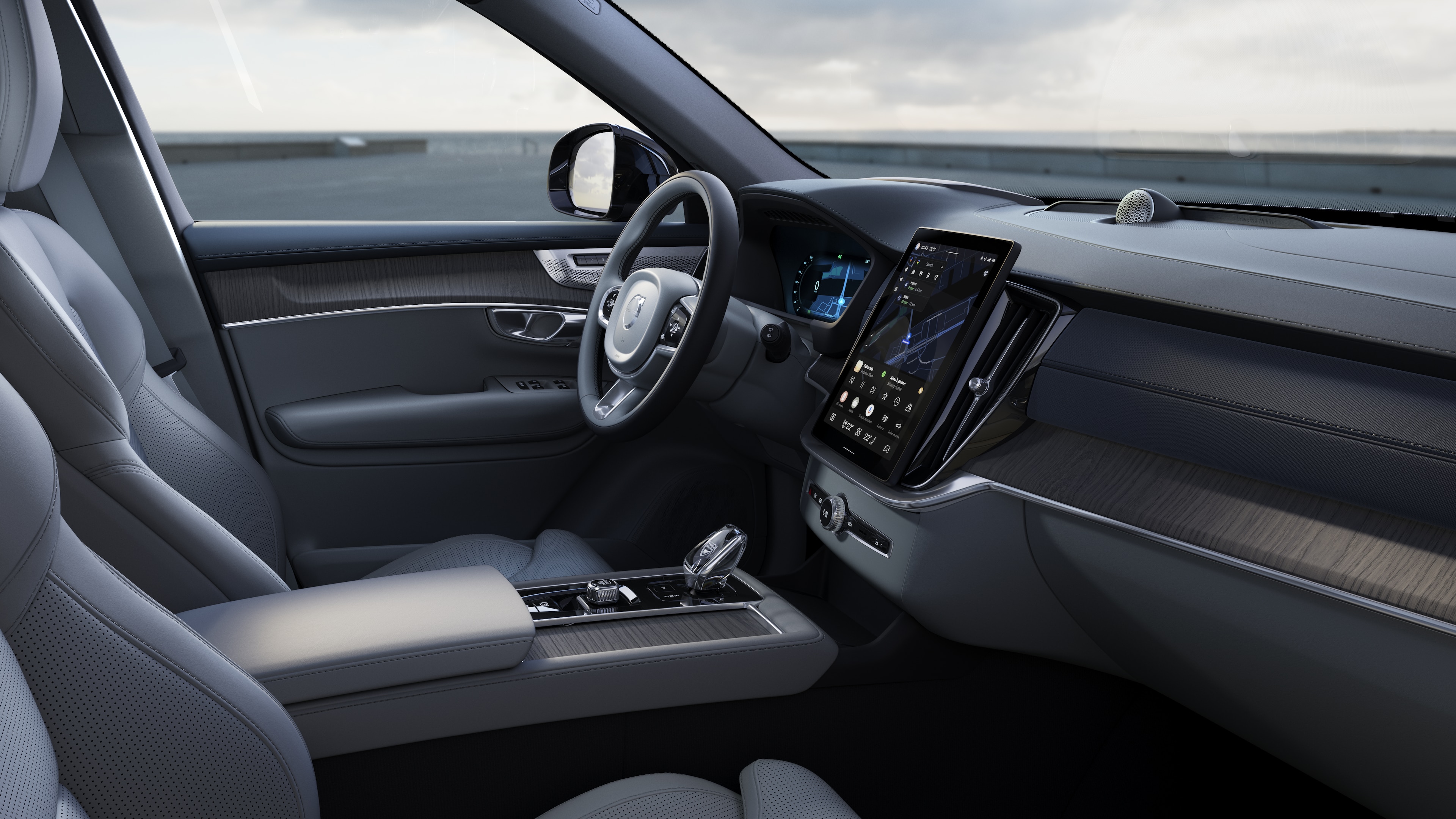 Interior del vehículo Volvo que muestra el salpicadero, el volante y la consola central con pantalla digital en un fondo de carretera abierta.