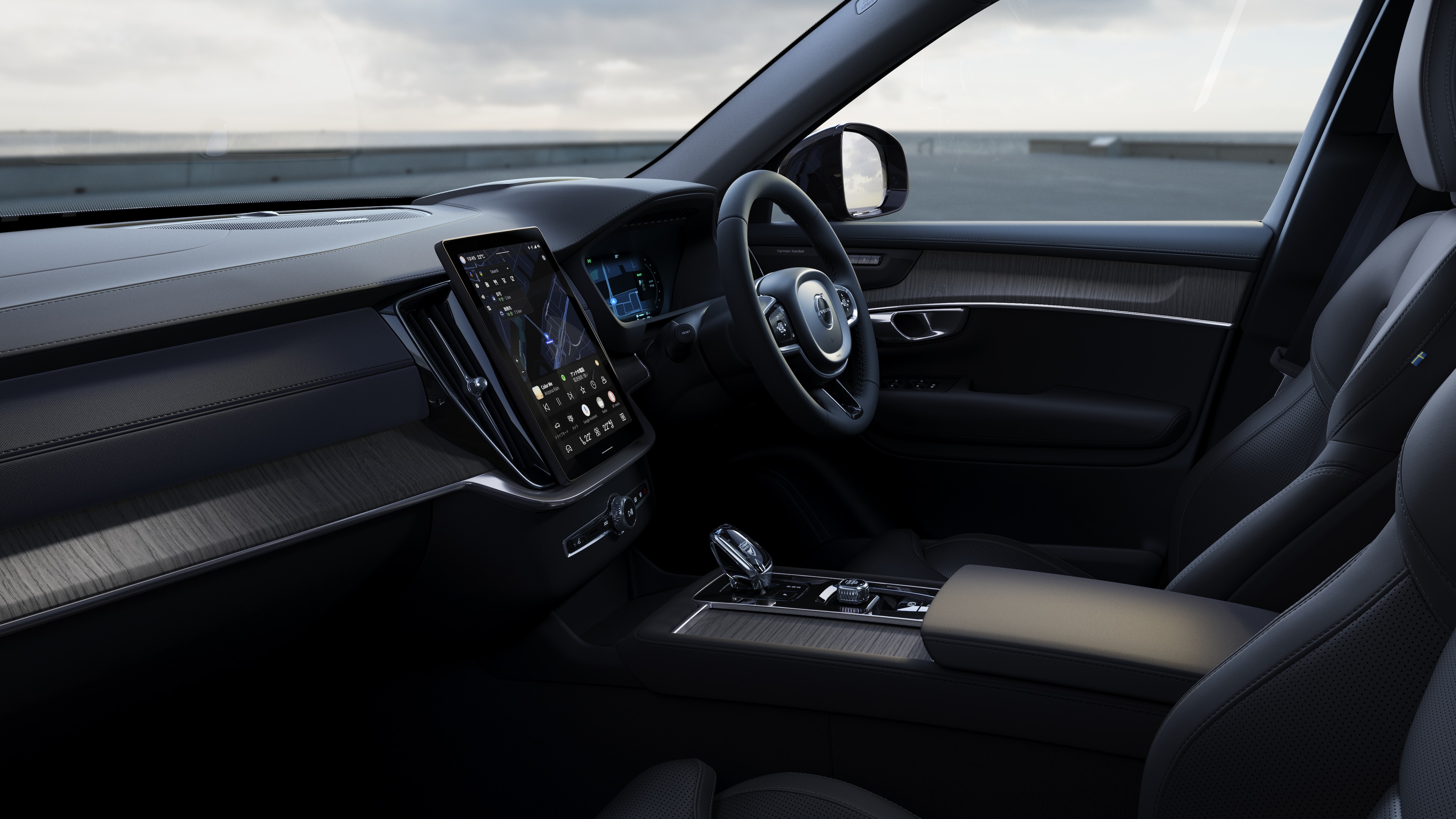 開けた路面を背景にダッシュボード、ステアリングホイール、センターコンソールをデジタルディスプレイで捉えたボルボ車のインテリア。
