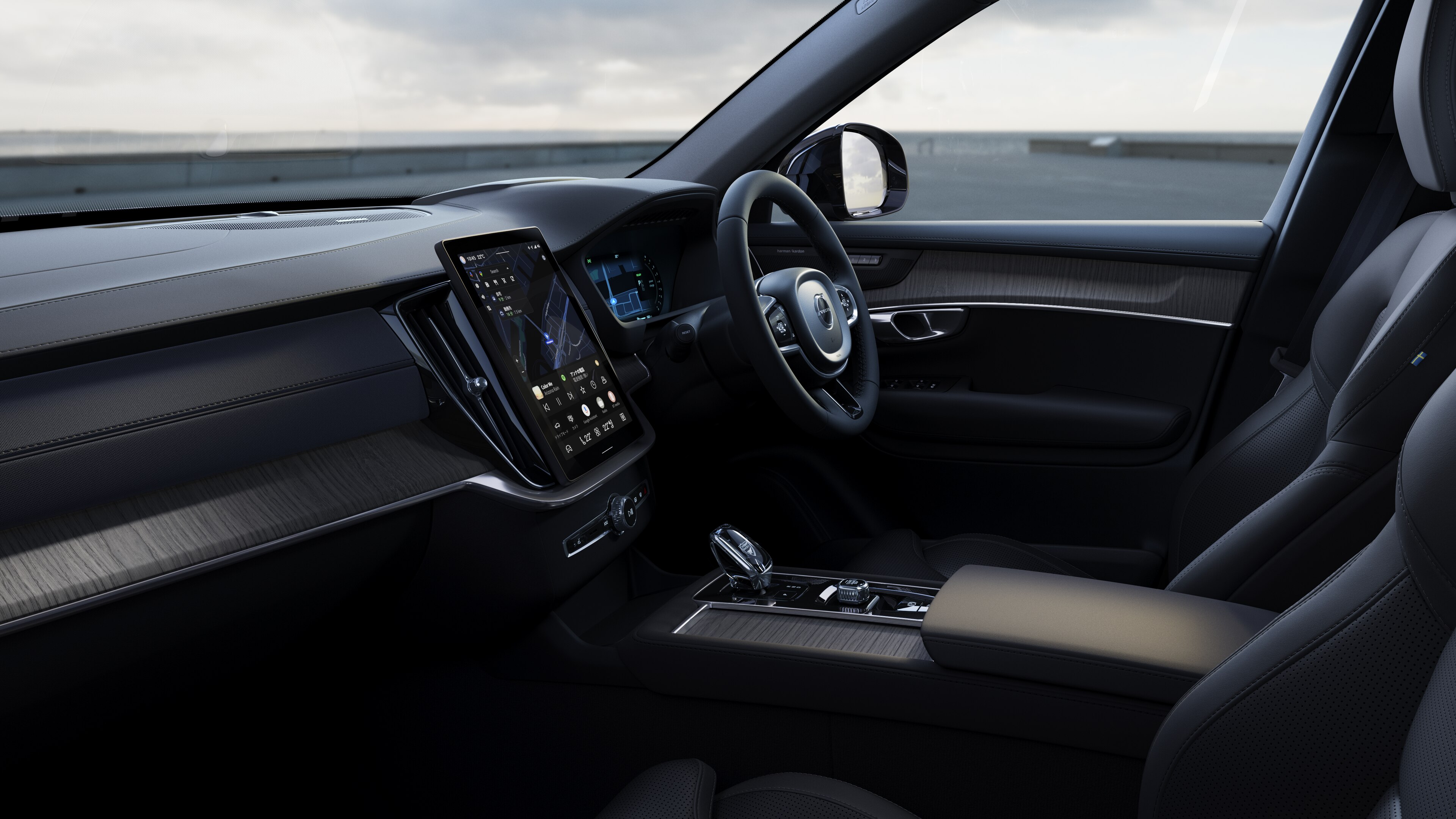 開けた路面を背景にダッシュボード、ステアリングホイール、センターコンソールをデジタルディスプレイで捉えたボルボ車のインテリア。