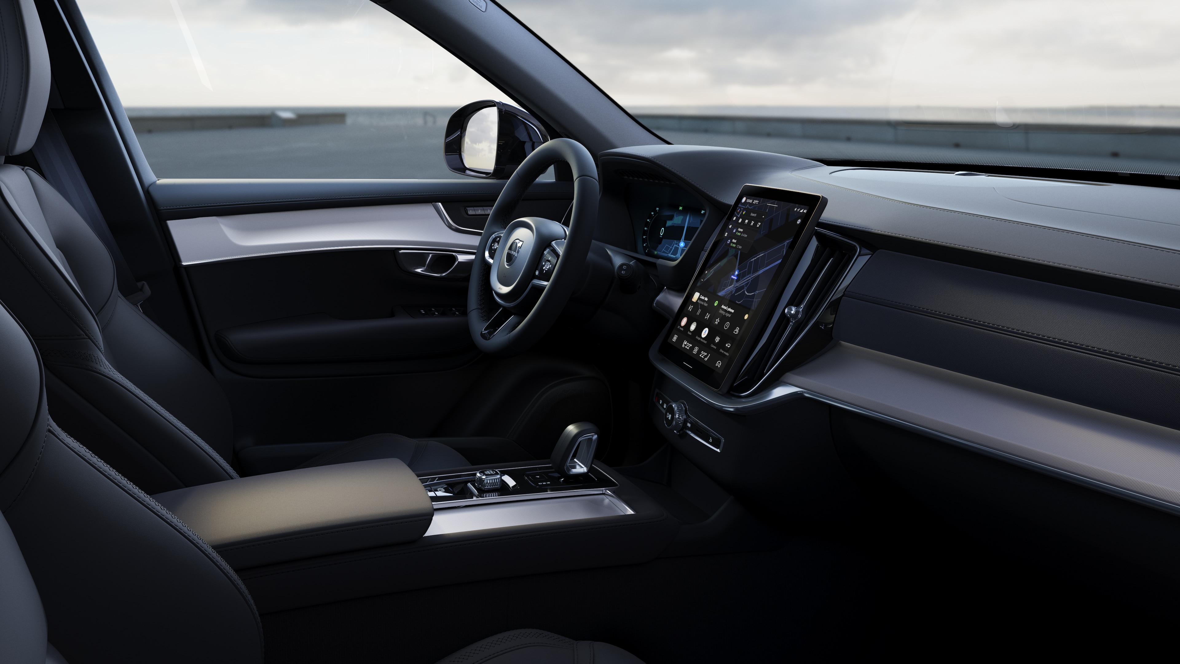 Interno di un'auto Volvo che mostra cruscotto, volante e console centrale con display digitale sullo sfondo di una strada aperta.