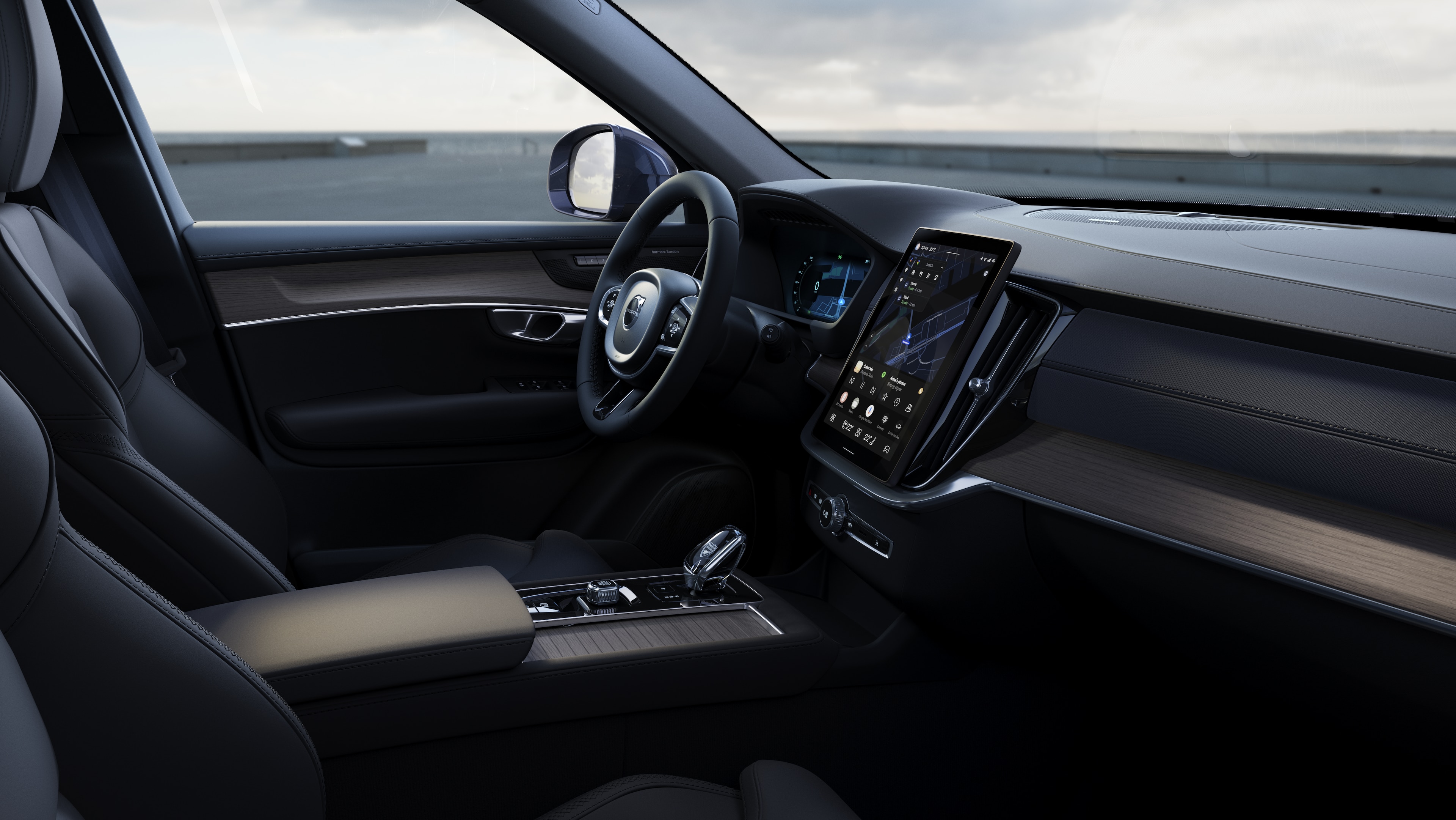 Interno di un'auto Volvo che mostra cruscotto, volante e console centrale con display digitale sullo sfondo di una strada aperta.