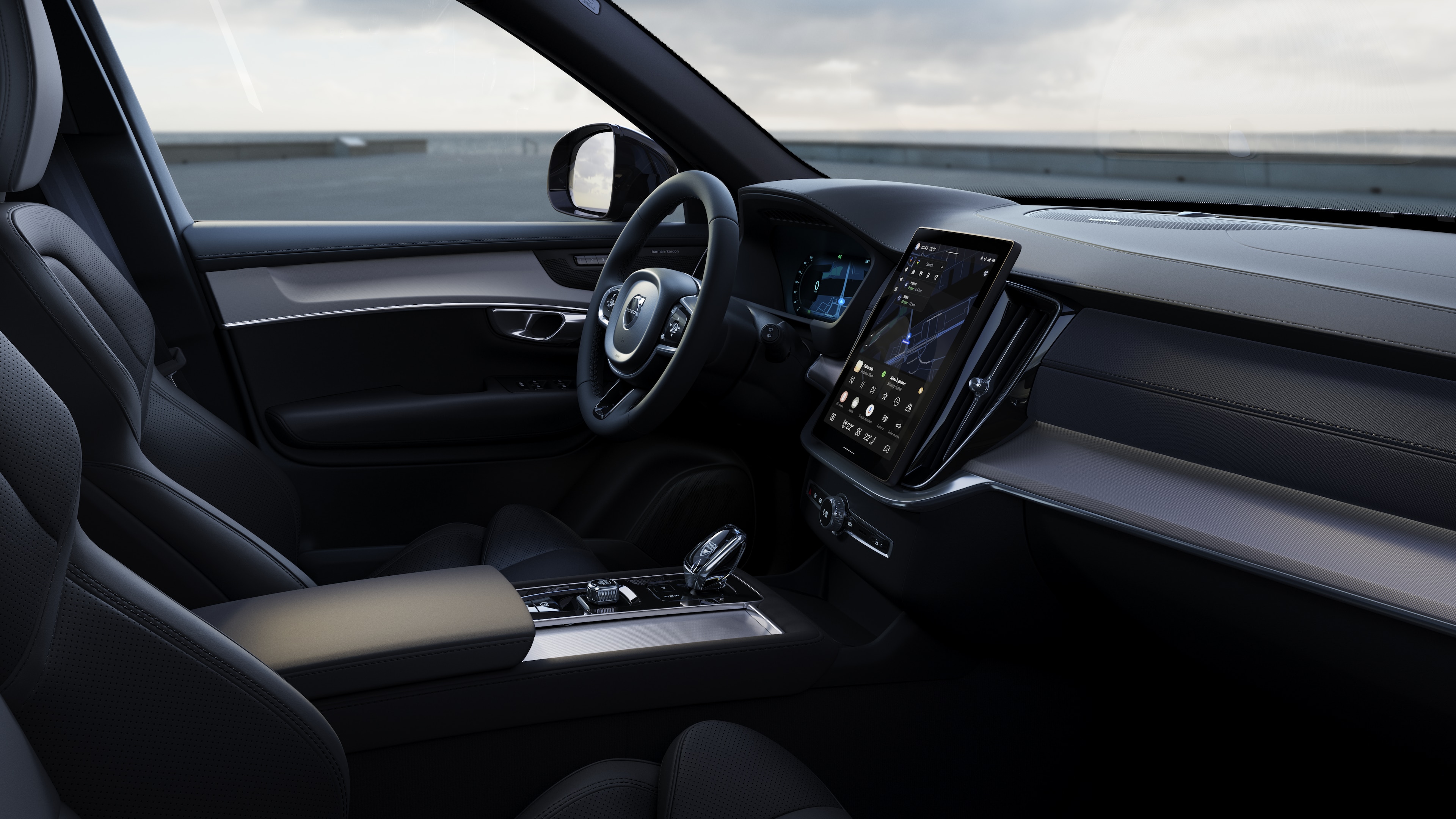 Interiér vozu Volvo zobrazující palubní desku, volant a středovou konzolu s digitálním displejem na pozadí otevřené silnice.