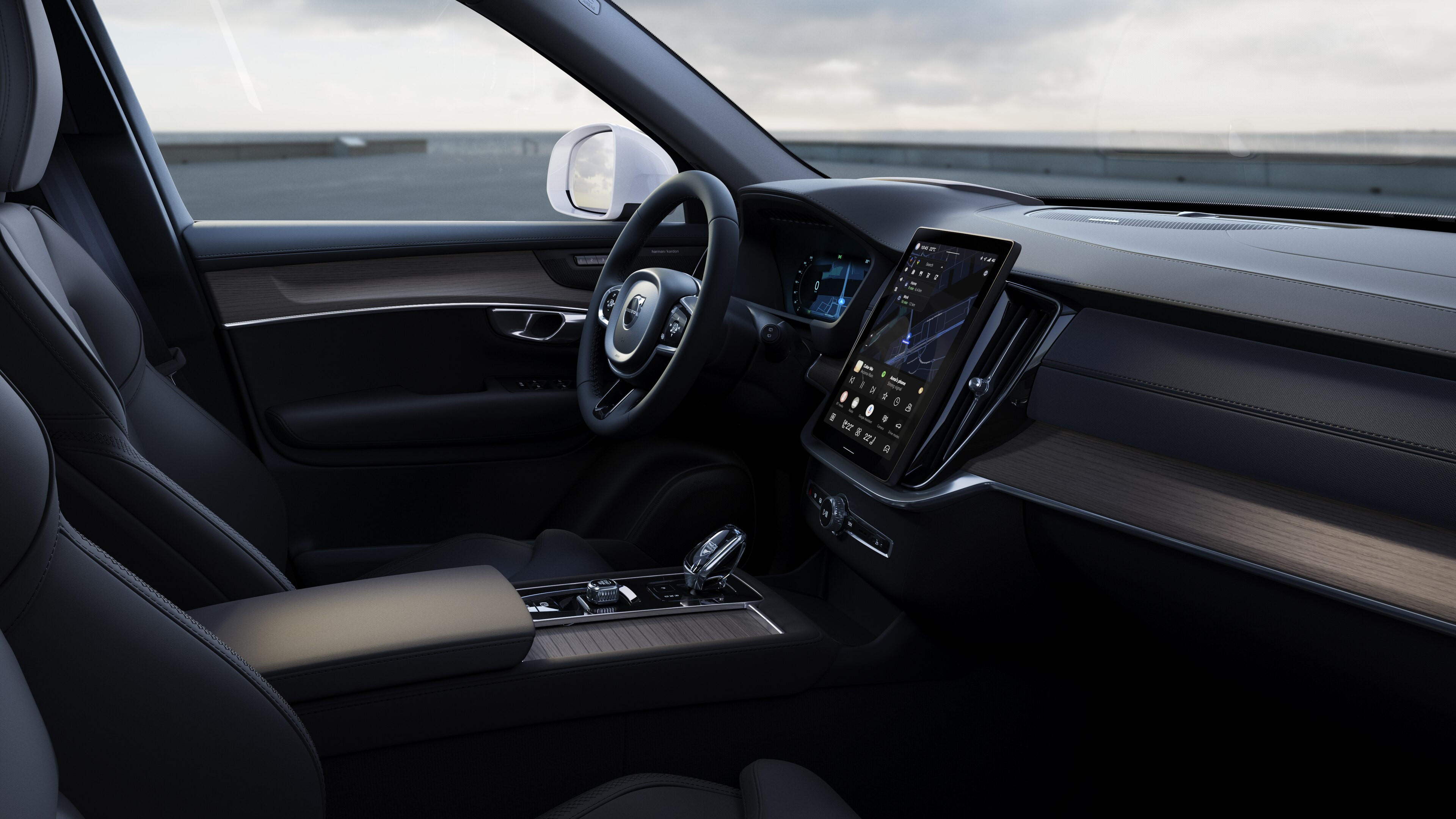 Interno di un'auto Volvo che mostra cruscotto, volante e console centrale con display digitale sullo sfondo di una strada aperta.