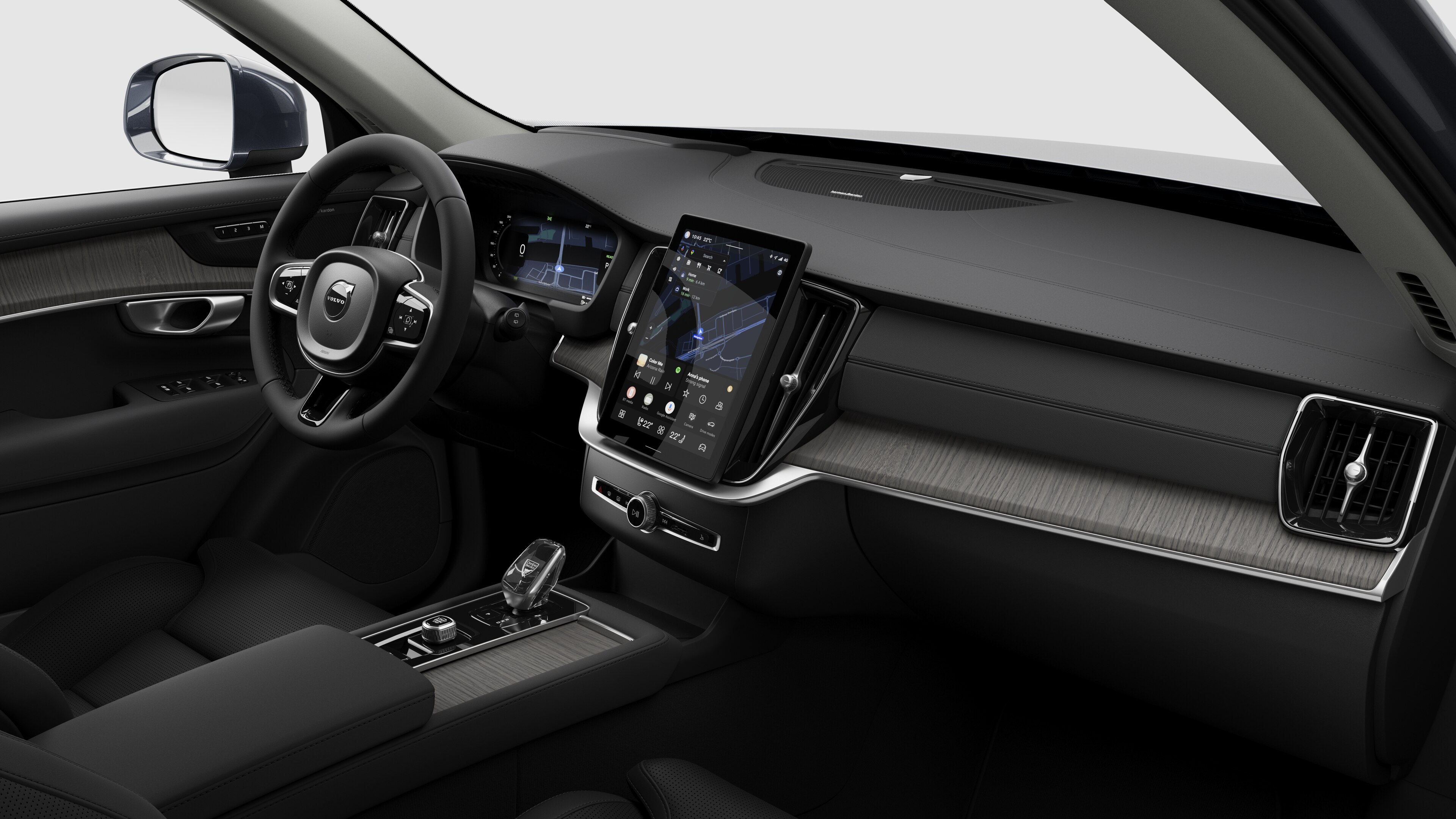 Interior view of a Volvo car showing the dashboard, steering wheel, center console, and digital display screen in a plain studio background.