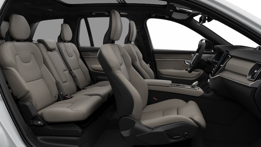 Widok z boku wnętrza samochodu Volvo z przednimi fotelami, tylnymi siedzeniami pasażera, kierownicą, deską rozdzielczą i konsolą środkową na tle zwykłego studia.