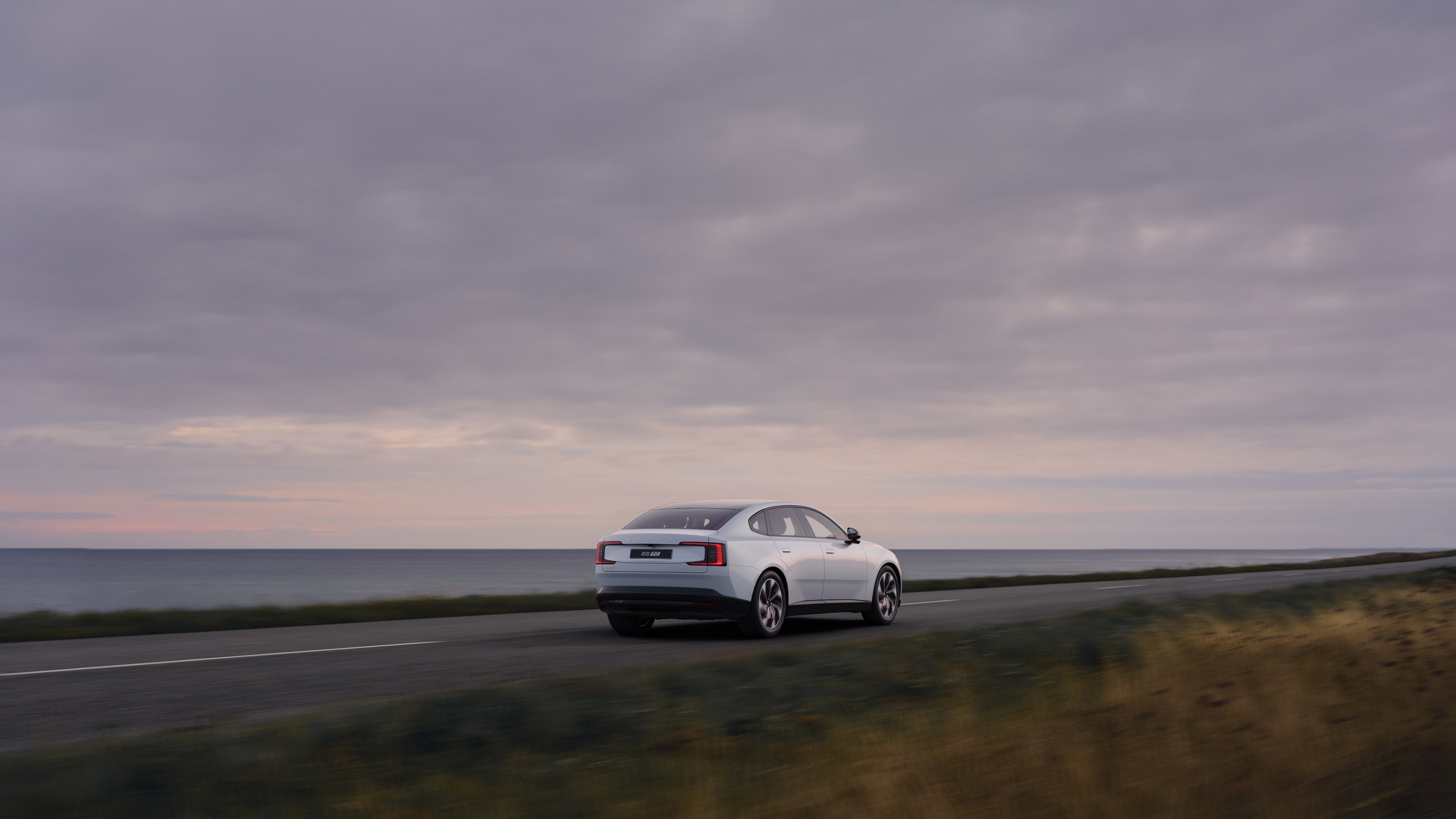 Volvo car rear view on a winding coastal road with a beachside background.