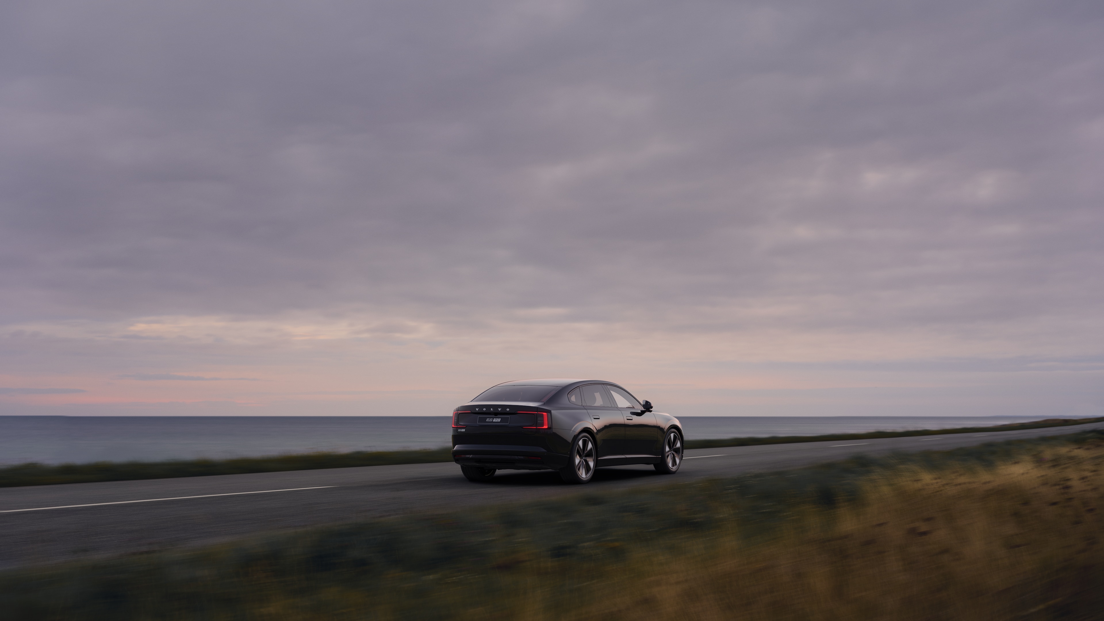 Volvo car rear view on a winding coastal road with a beachside background.