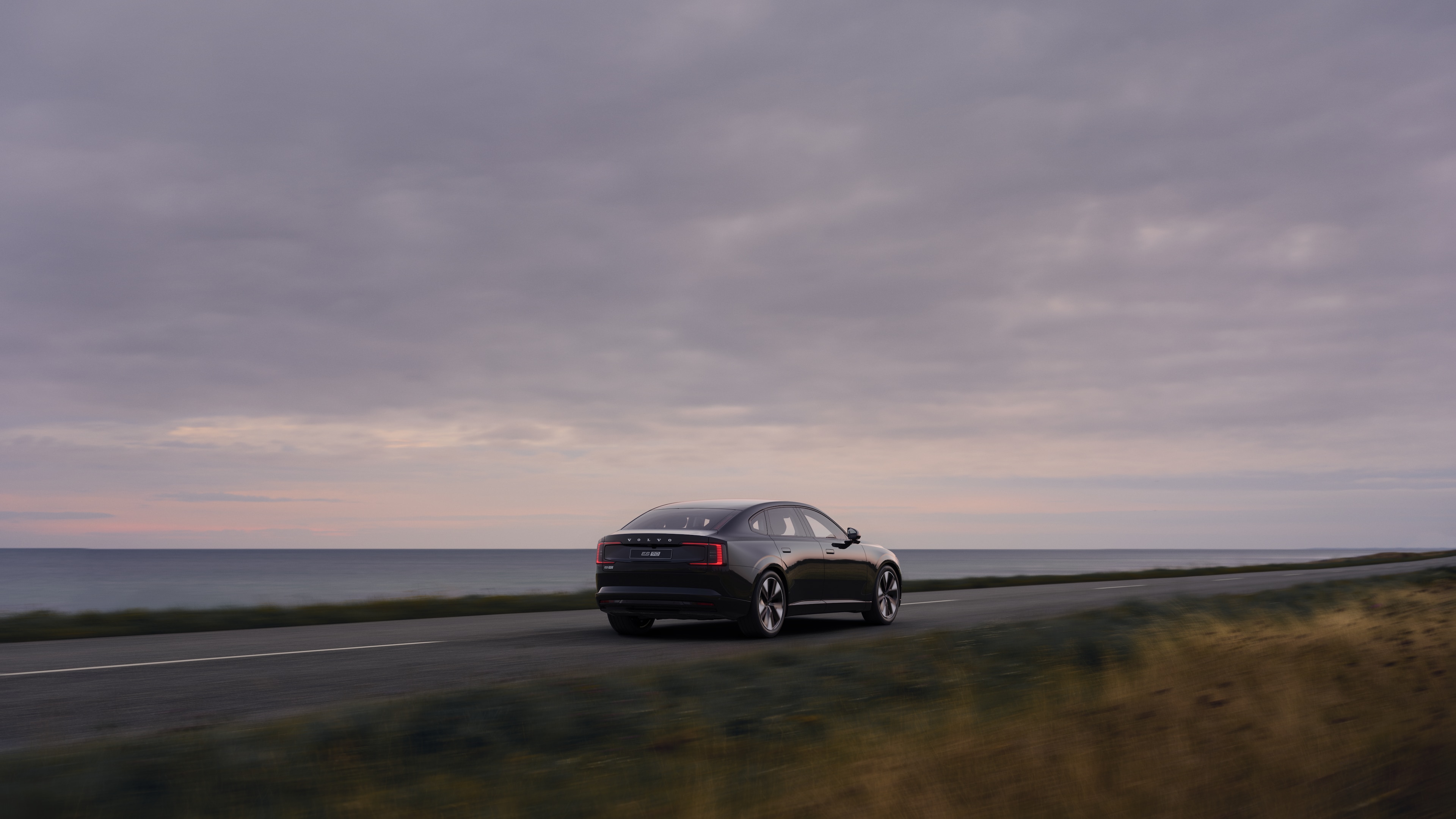 Volvo car rear view on a winding coastal road with a beachside background.
