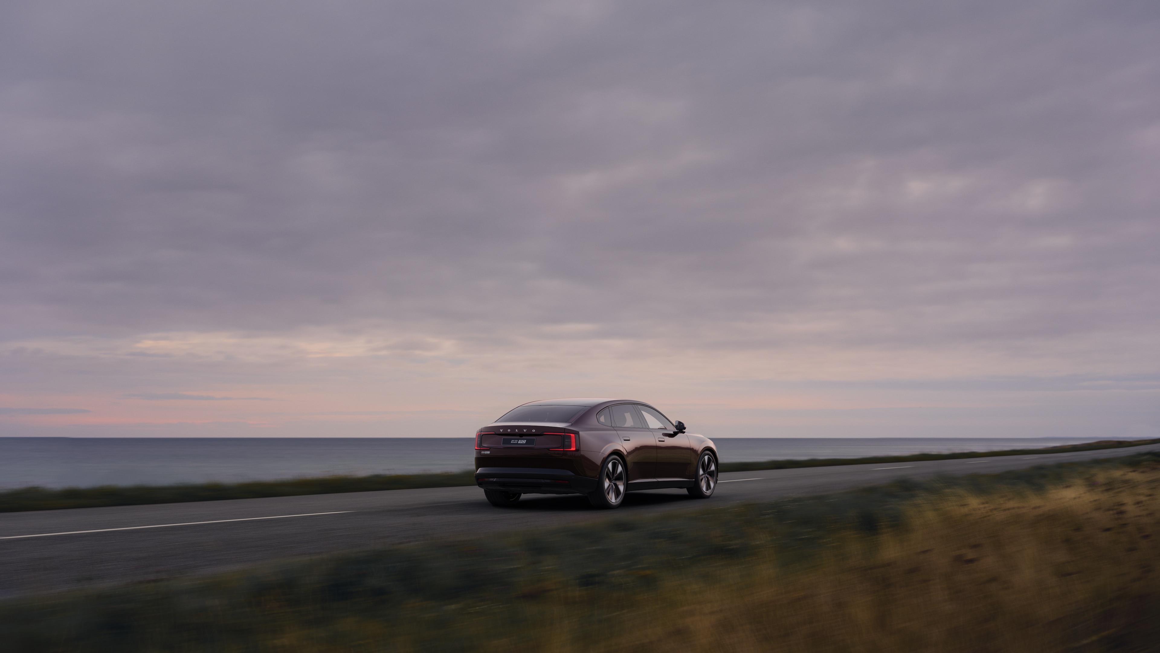 Volvo car rear view on a winding coastal road with a beachside background.