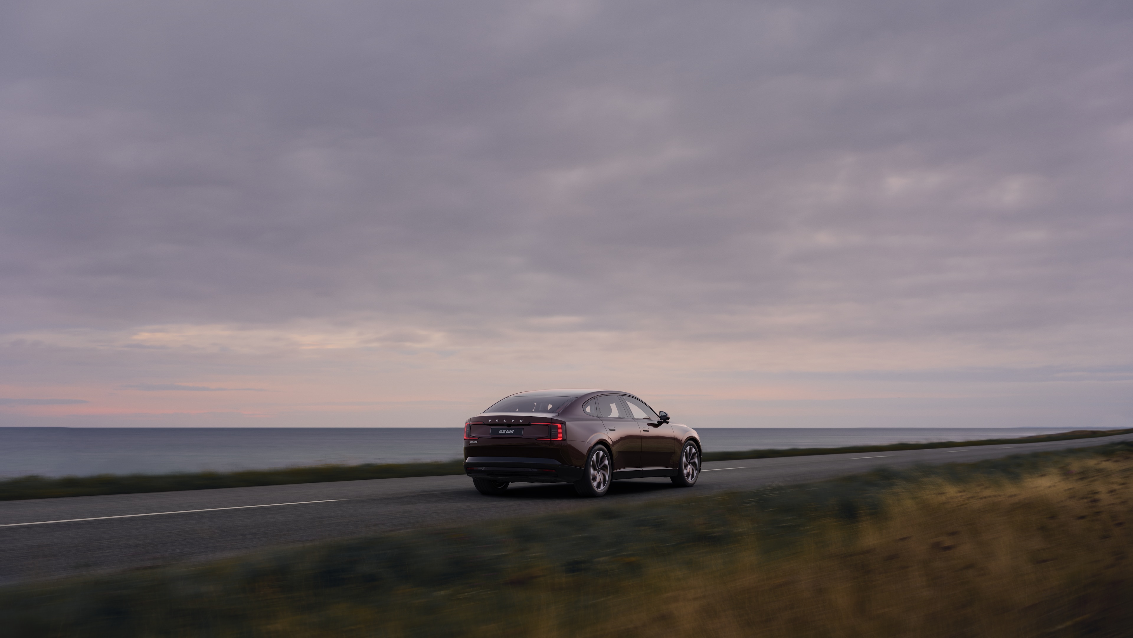 Volvo car rear view on a winding coastal road with a beachside background.