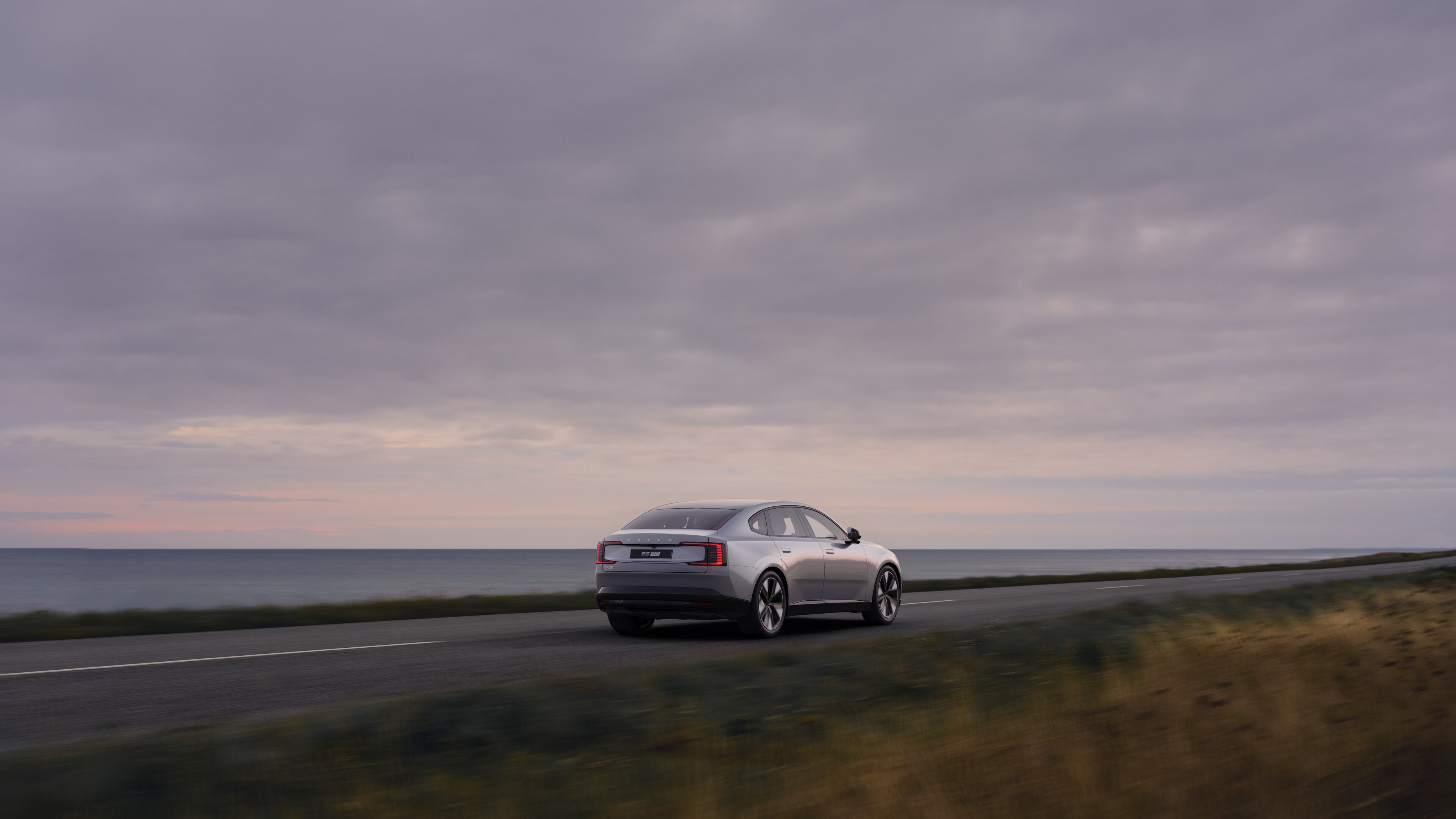 Volvo car rear view on a winding coastal road with a beachside background.