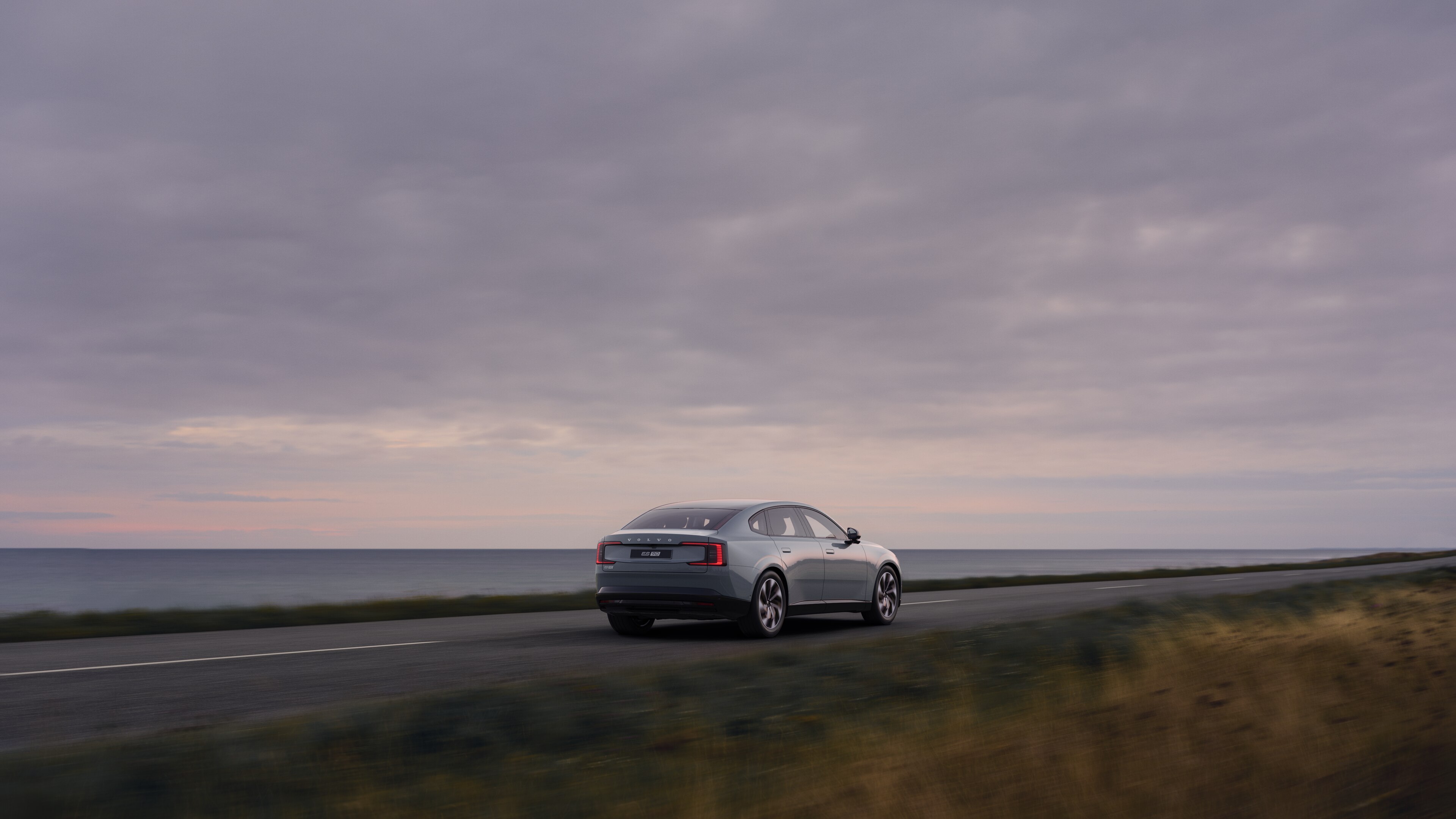Изглед отзад на автомобил Volvo на криволичещ крайбрежен път с фон на плажа.