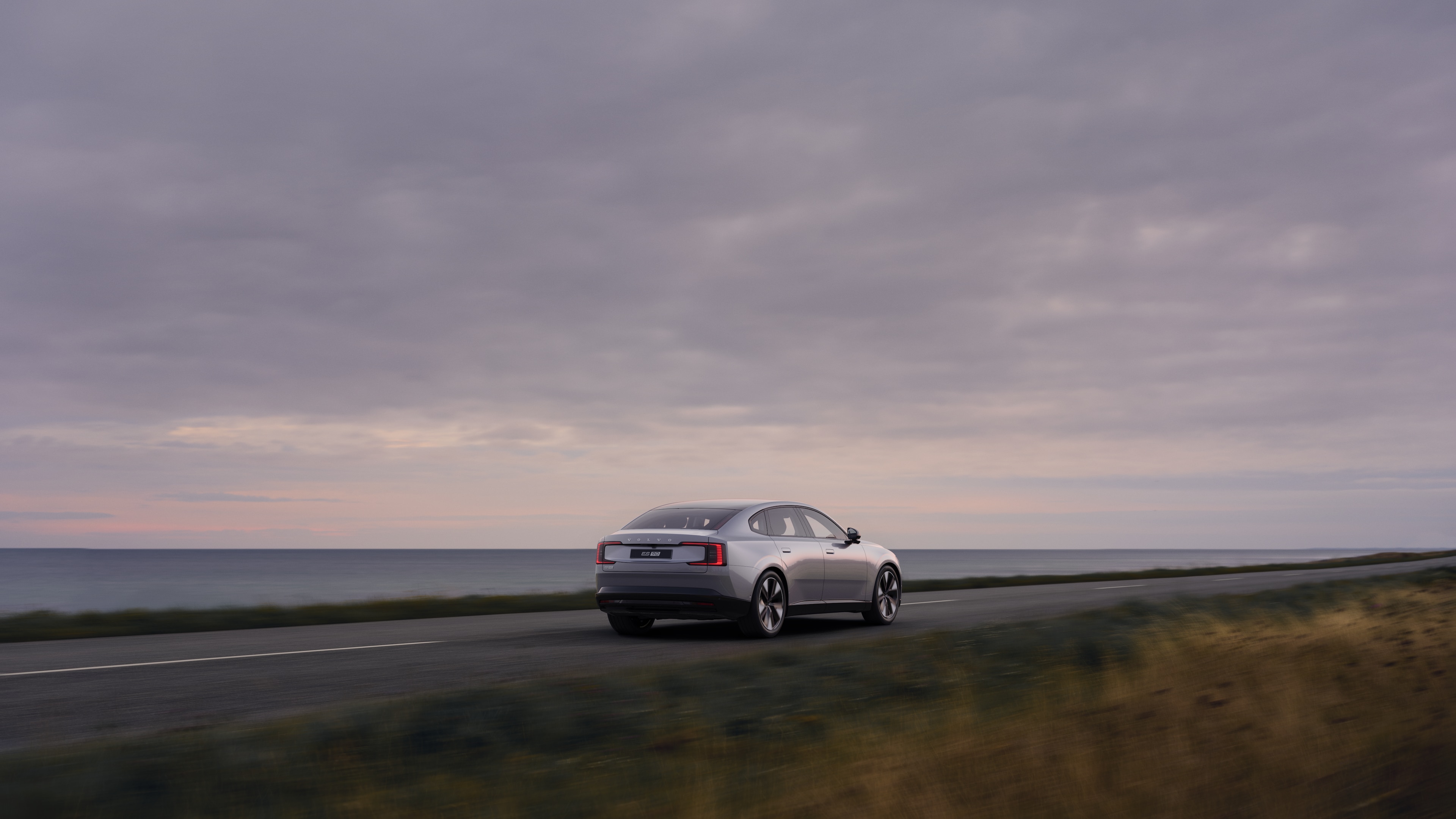 Vista trasera de un coche Volvo en una sinuosa carretera costera con un fondo junto a la playa.