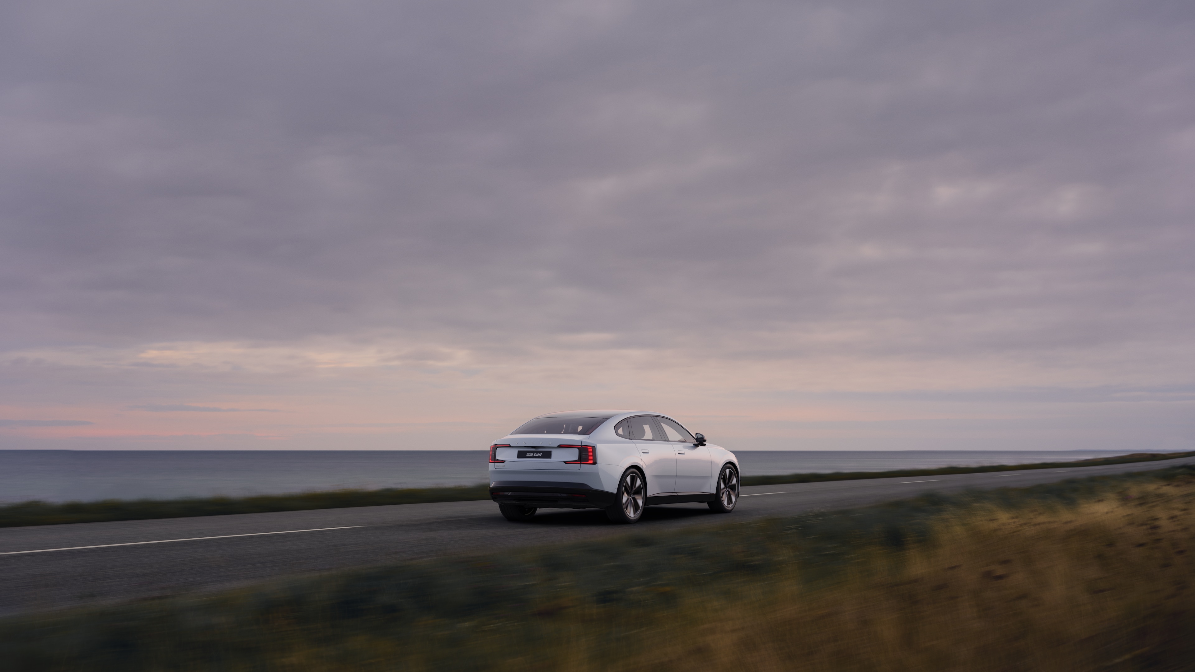 Vy bakifrån av en Volvo på en slingrande kustväg med en strandbakgrund.