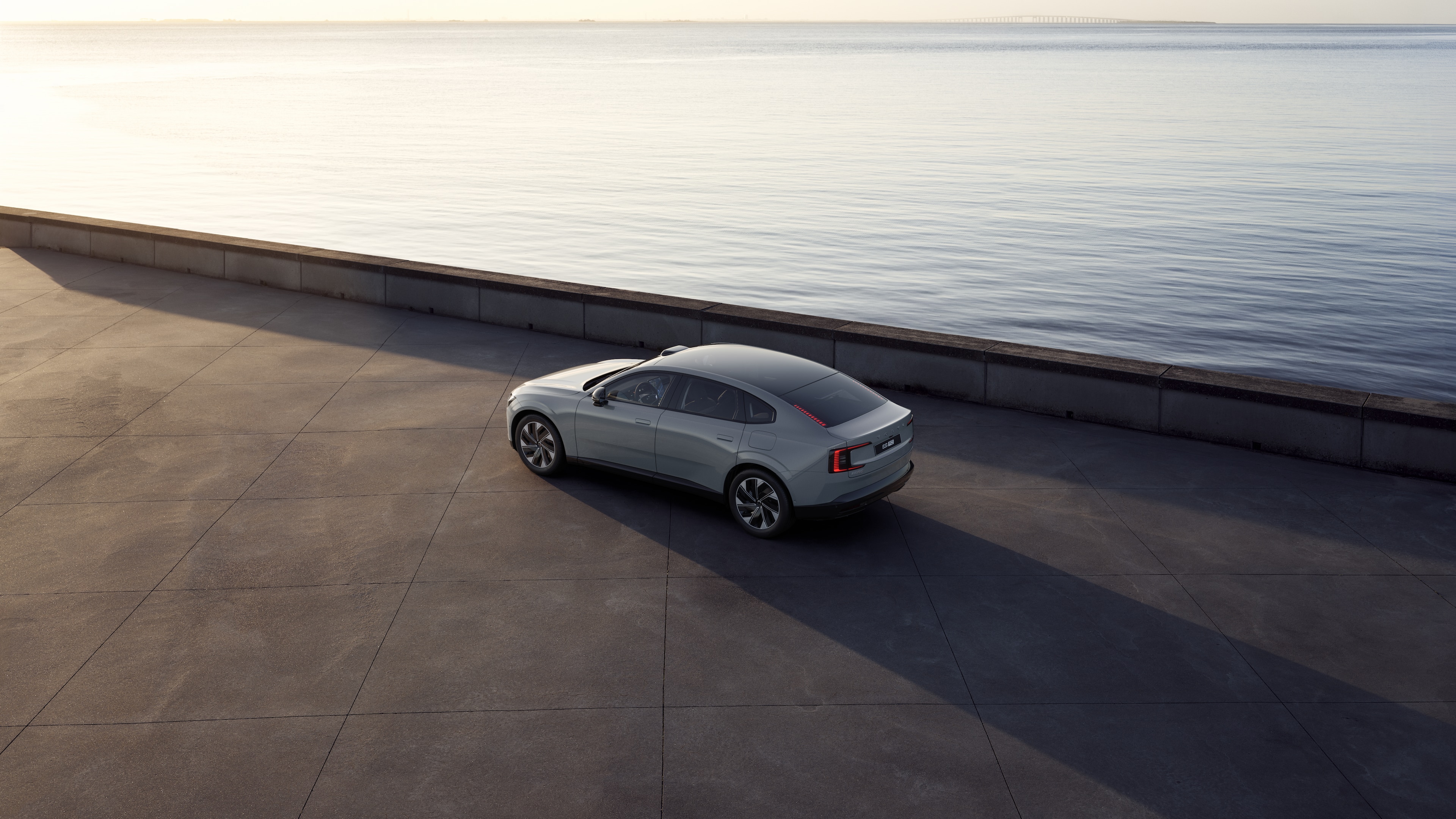 Автомобил Volvo отзад с изглед от три четвърти, паркиран до бетонна стена на фона на градска улица.