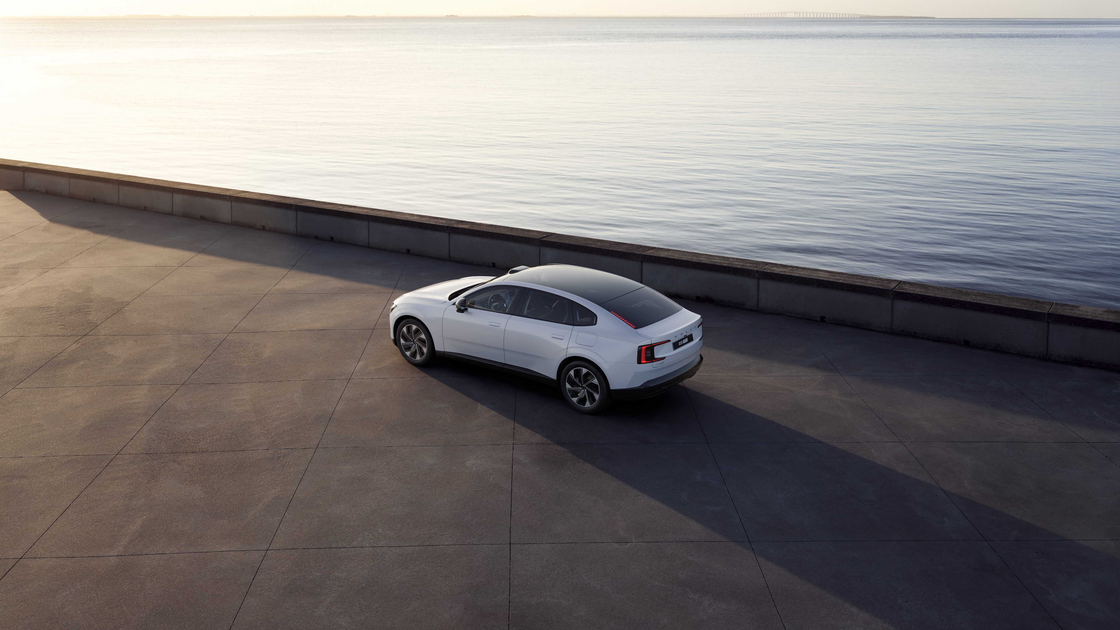 Volvo car in rear three-quarter view parked against a concrete wall on an urban street background.