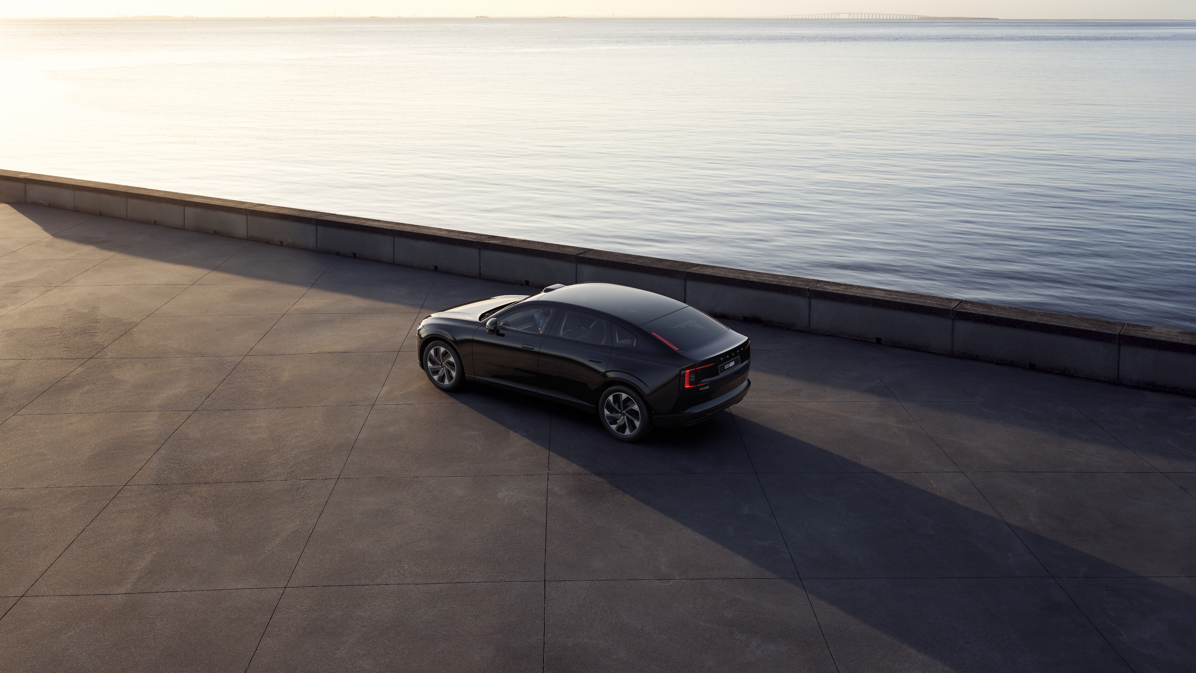 Volvo car in rear three-quarter view parked against a concrete wall on an urban street background.
