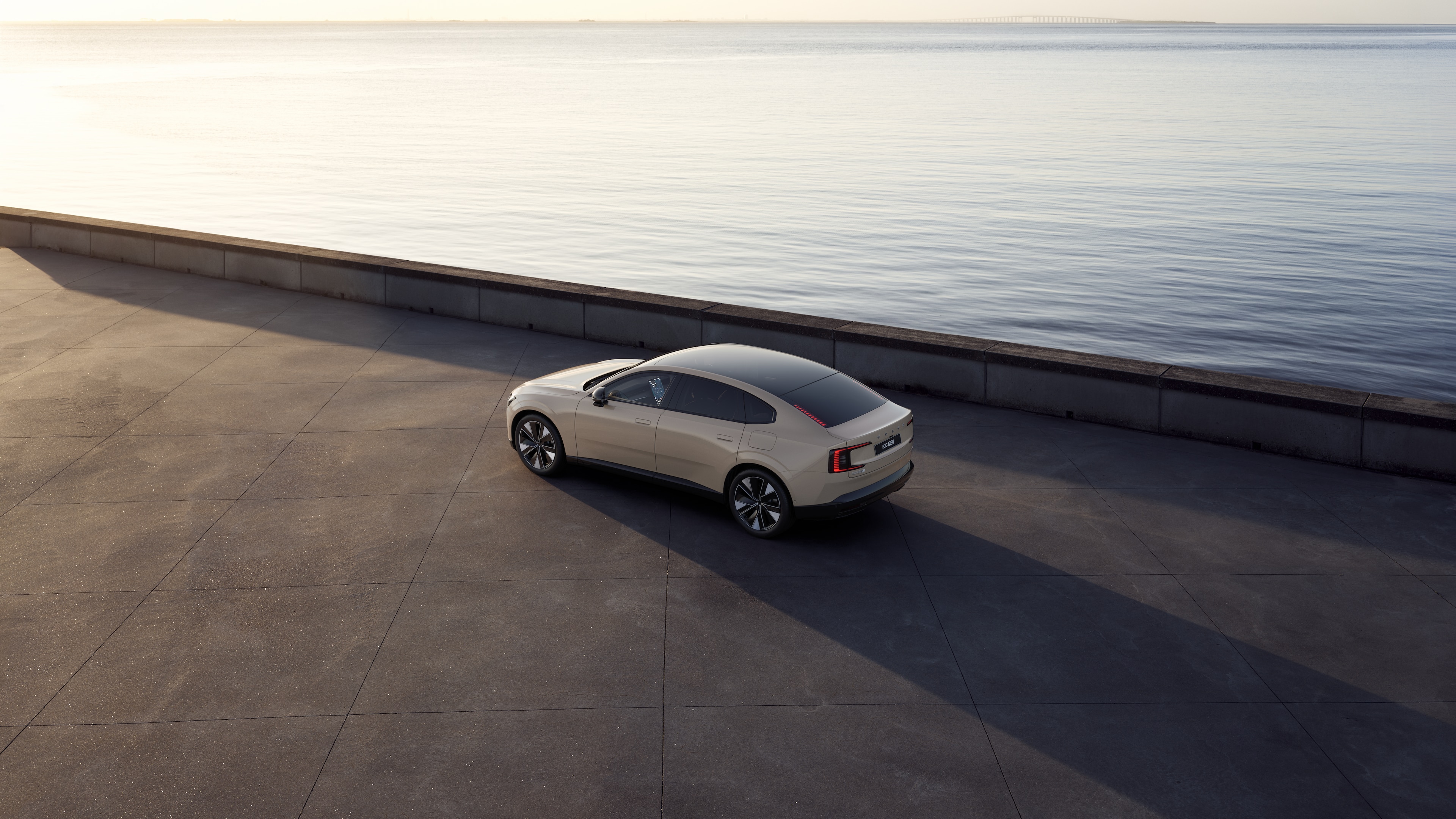 Volvo car in rear three-quarter view parked against a concrete wall on an urban street background.