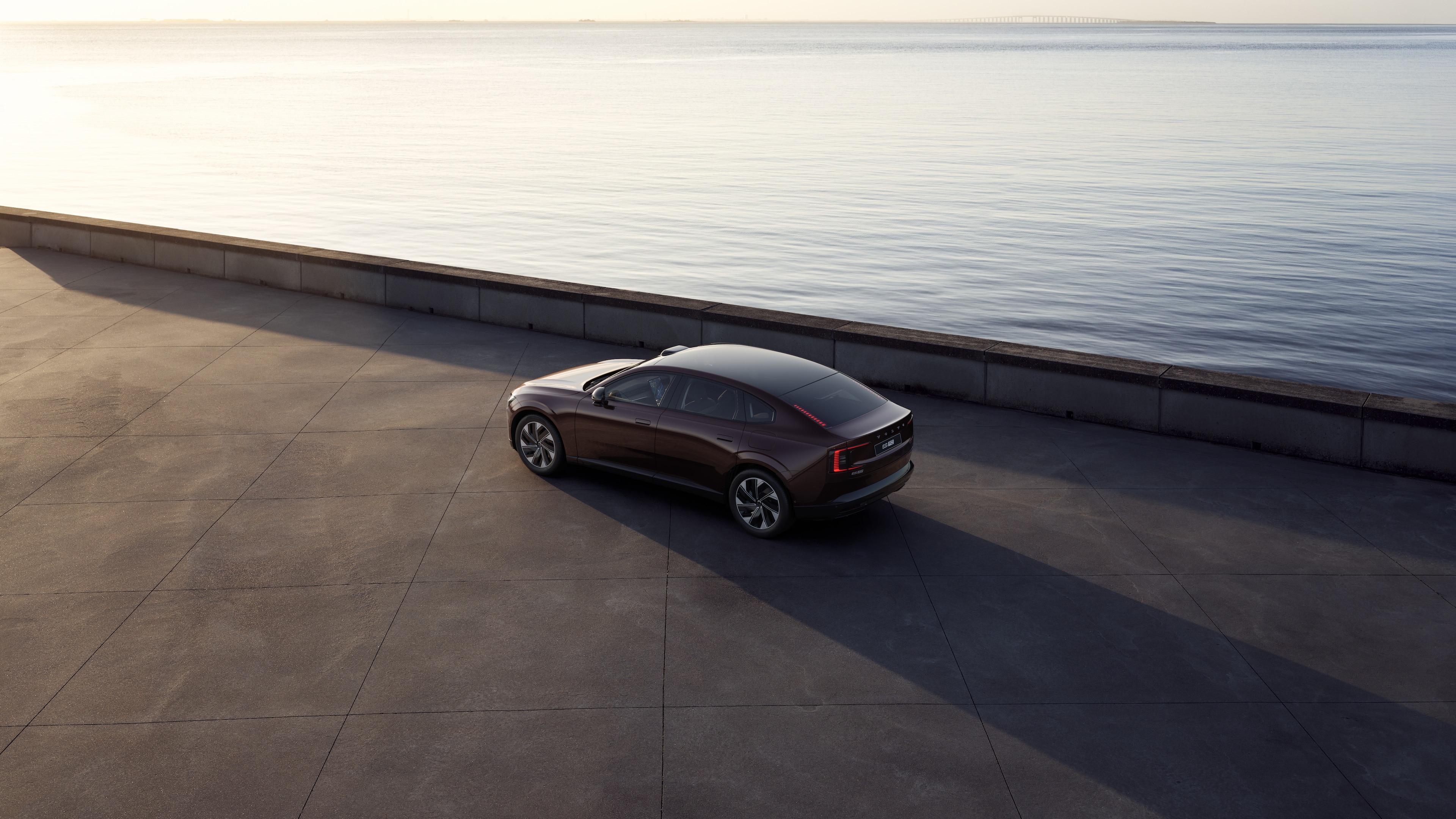 Volvo car in rear three-quarter view parked against a concrete wall on an urban street background.