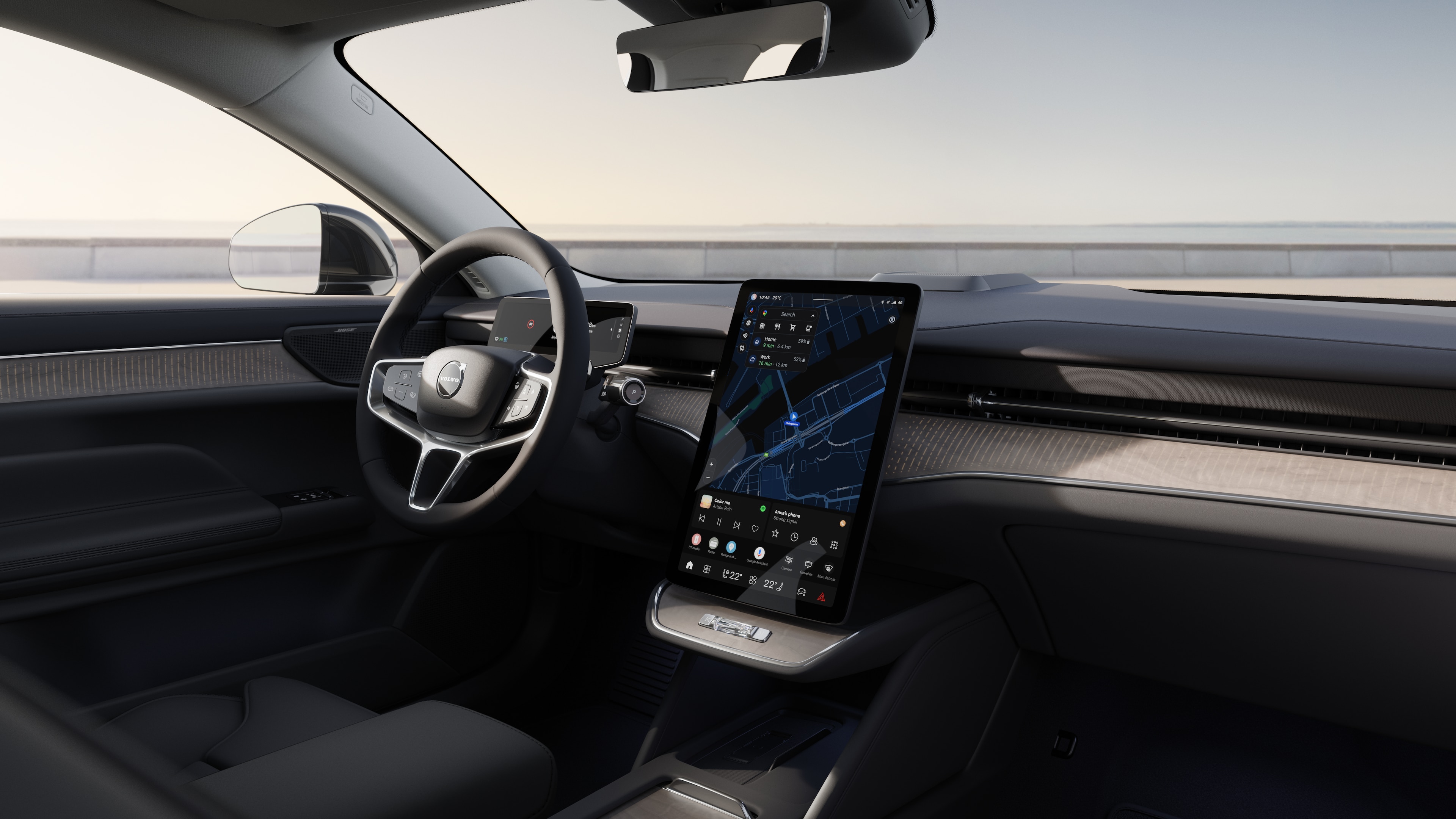 Interno di un'auto Volvo che mostra cruscotto, volante e console centrale con display digitale sullo sfondo di una strada aperta.