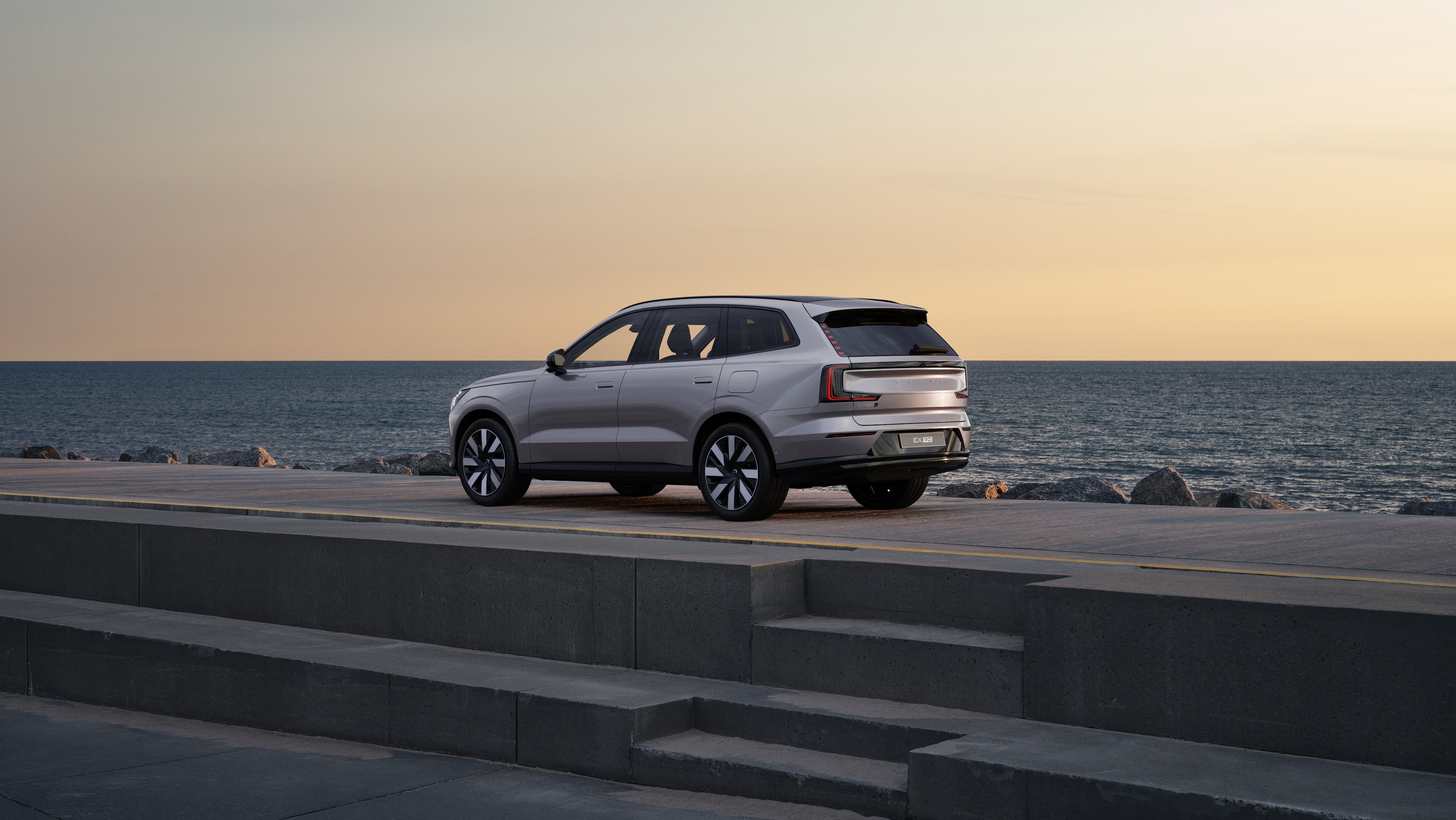 Volvo car in rear three-quarter view parked against a concrete wall on an urban street background.
