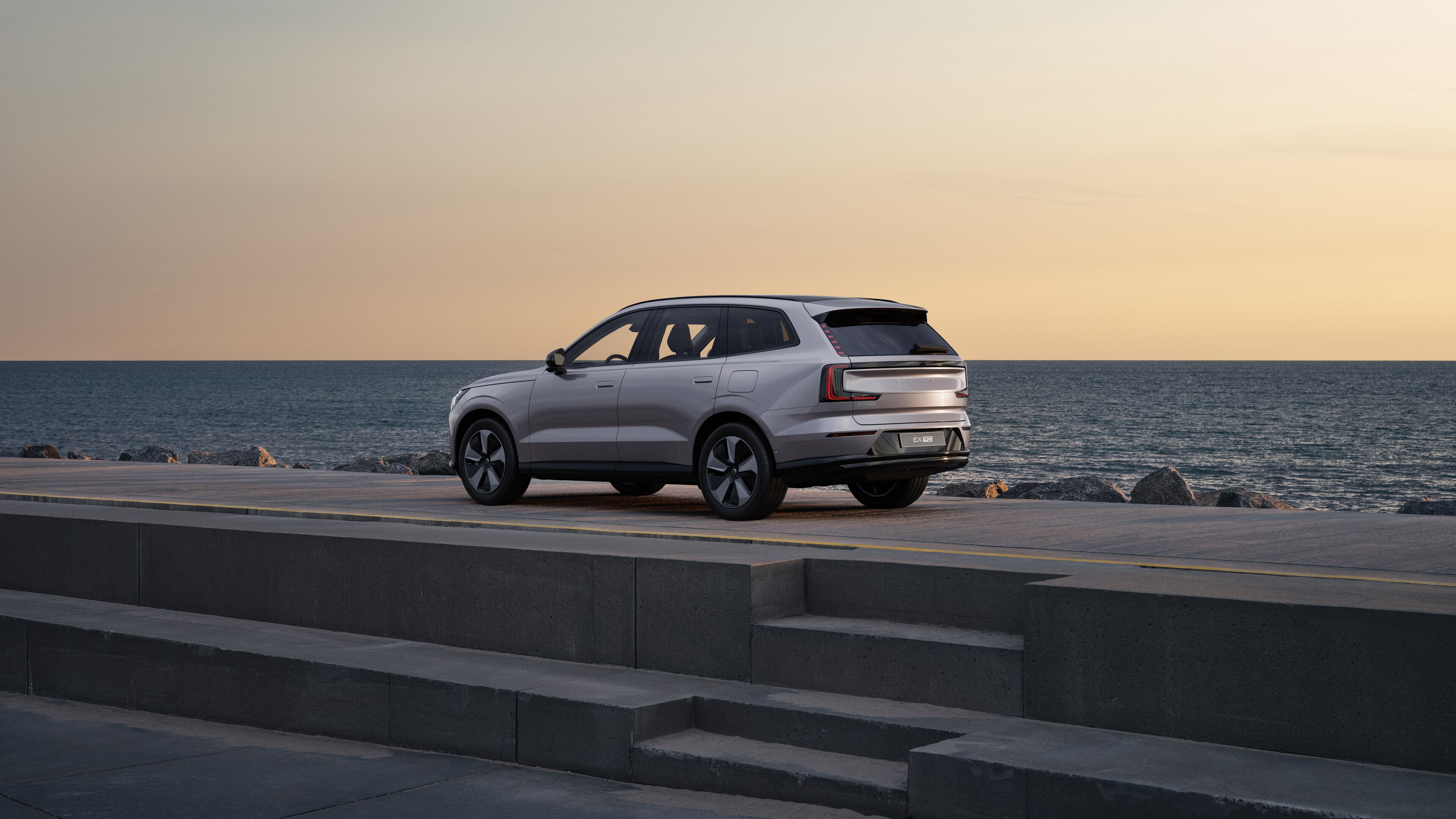 Volvo en vue arrière de trois quarts, garée contre un mur en béton dans une rue urbaine.