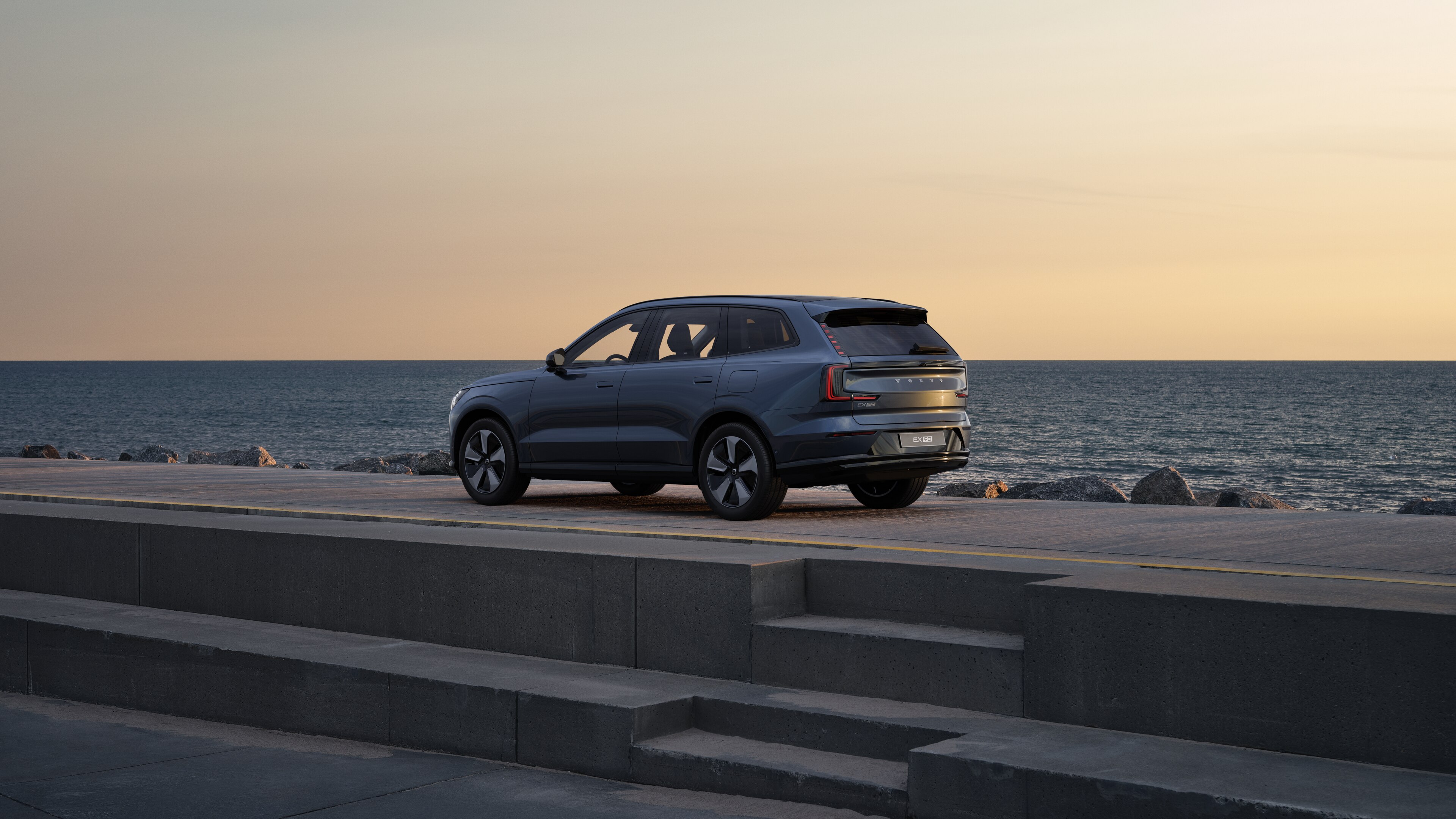 Volvo en vue arrière de trois quarts, garée contre un mur en béton dans une rue urbaine.