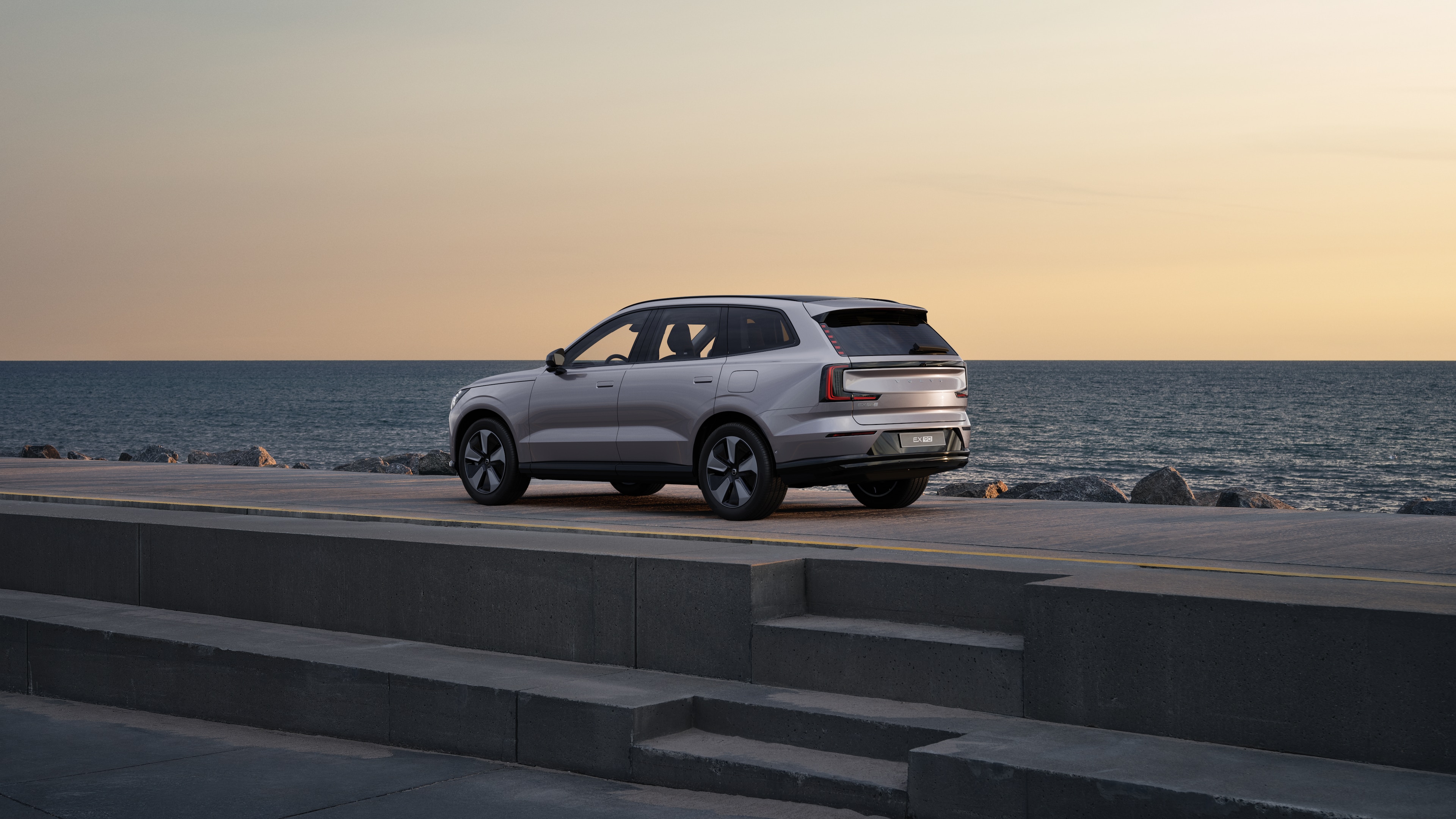 Trekvart visning av Volvo bak parkert mot en betongvegg i en urban gatebakgrunn.