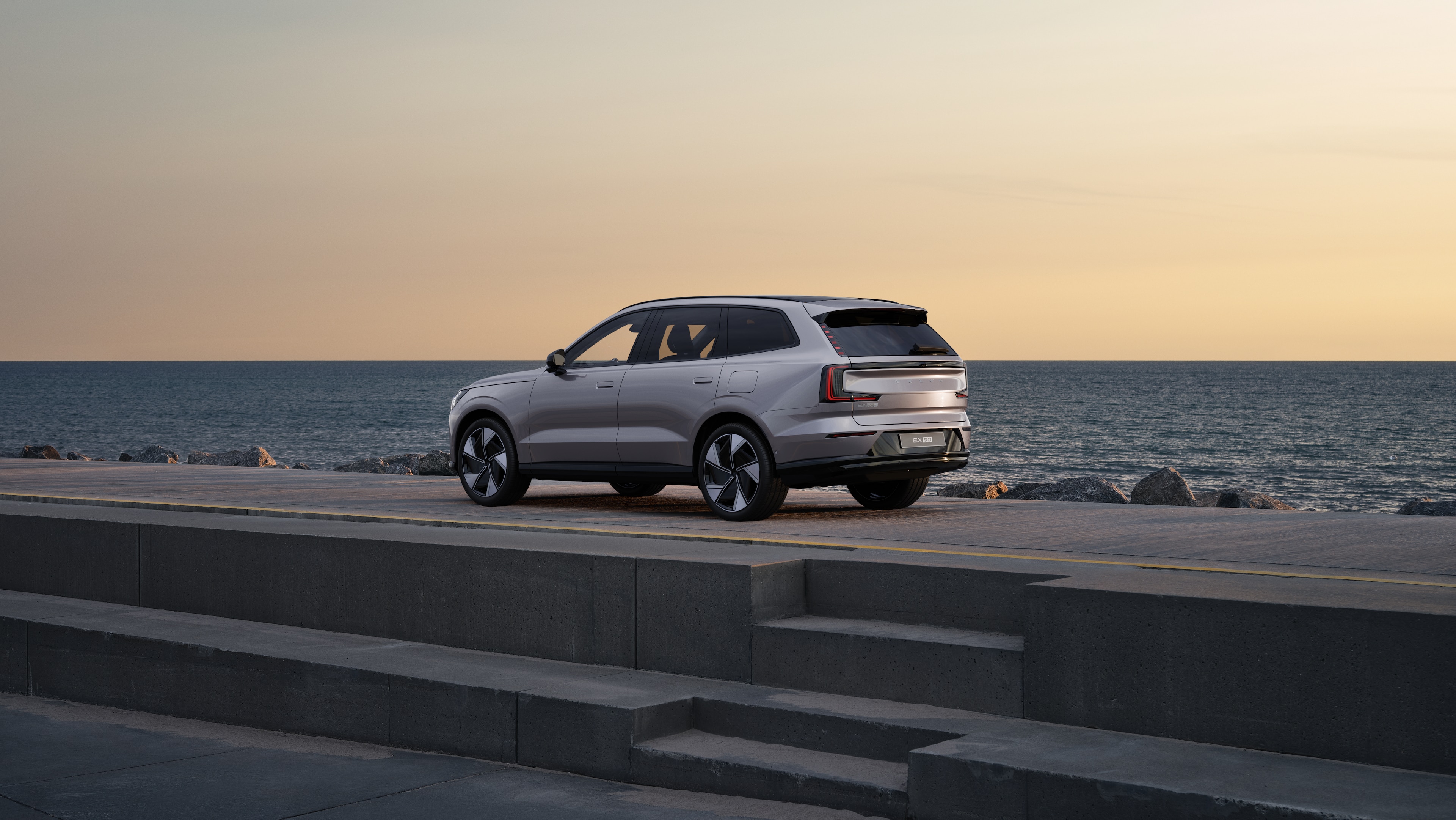 Volvo car in rear three-quarter view parked against a concrete wall on an urban street background.